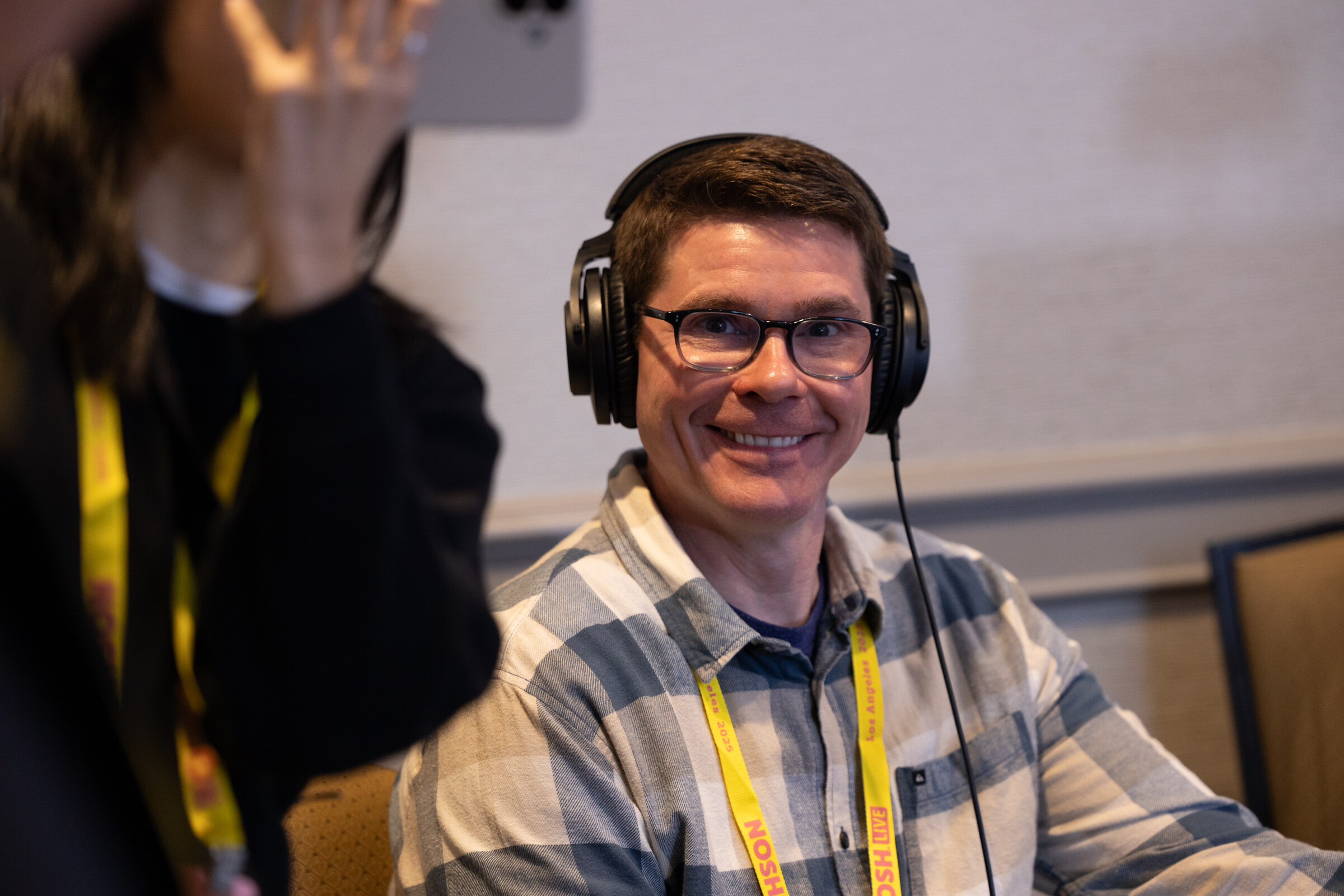 A smiling man wearing over-ear headphones and a yellow Nosh Live lanyard.