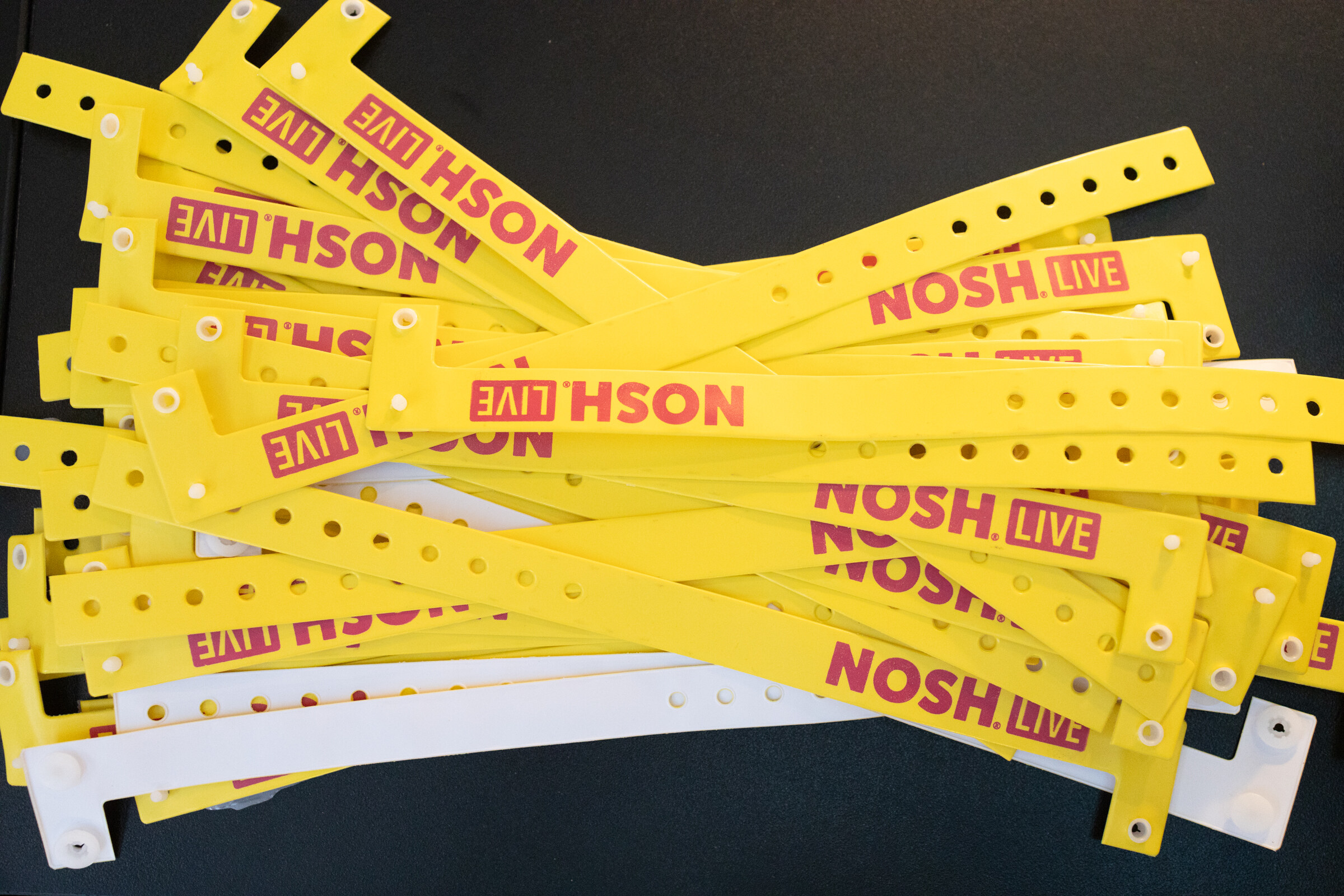 A pile of yellow and white plastic wristbands printed Nosh Live.
