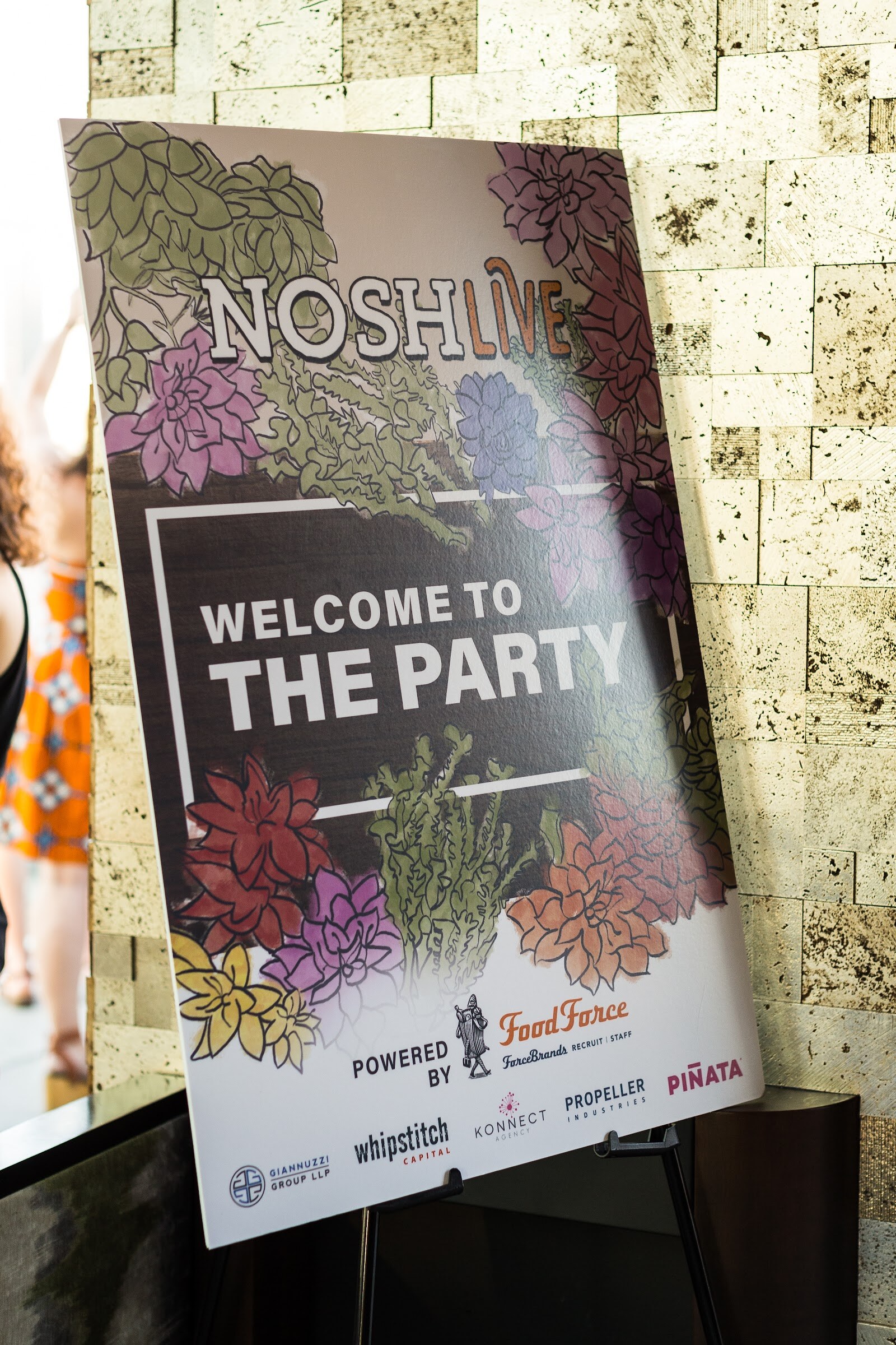 A printed sign on an easel reads Nosh Live Welcome to the Party, Powered by Food Force, with sponsor logos including Whipstitch Capital and Propeller Industries.