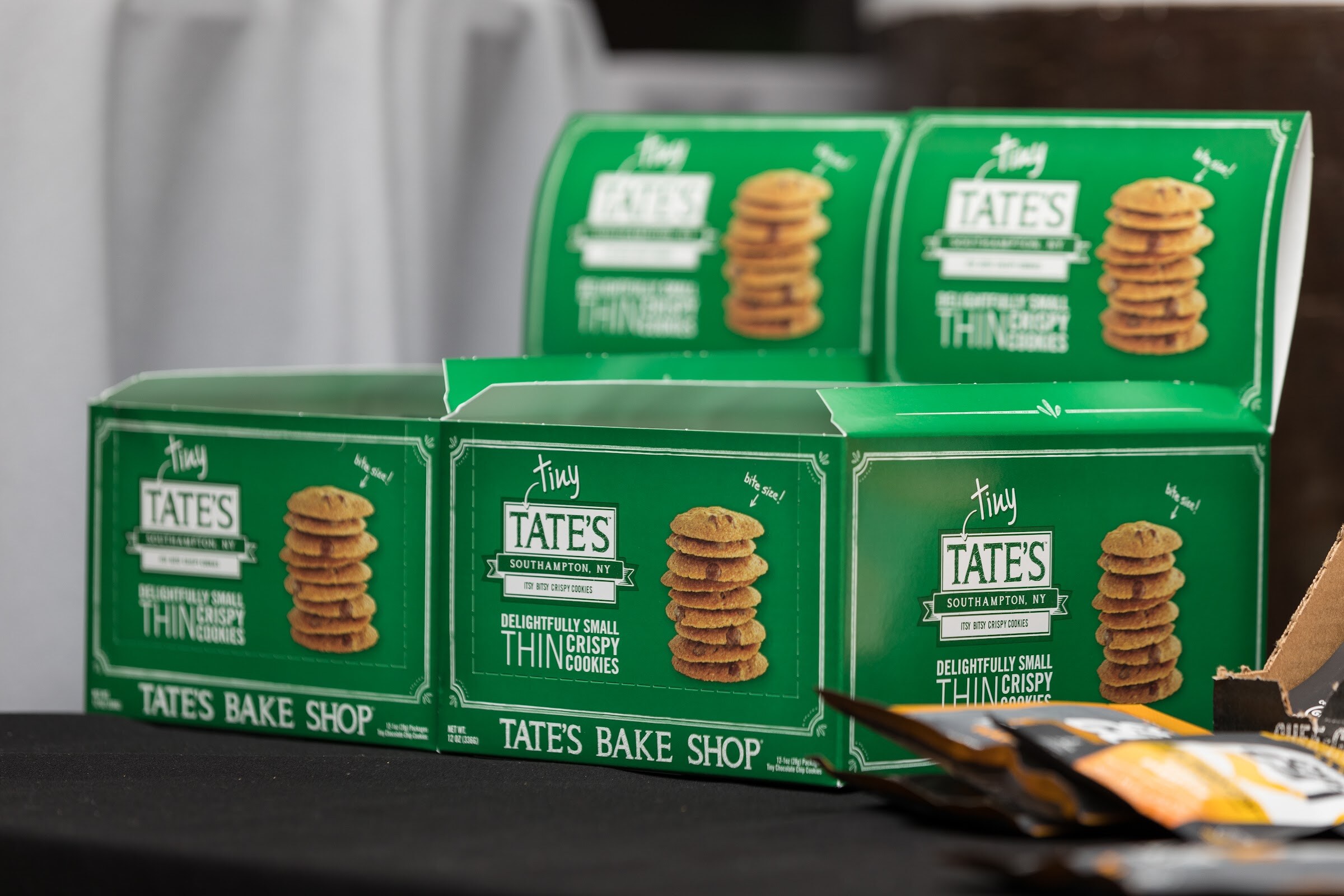 Open green cartons labeled Tate's Bake Shop Tiny Thin Crispy Cookies on a black table.