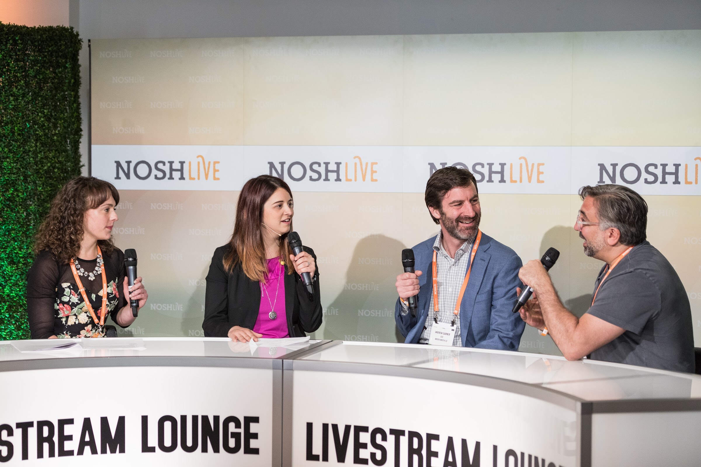 Four people with microphones sit at a curved white desk labeled Livestream Lounge in front of a Nosh Live backdrop and a hedge wall.