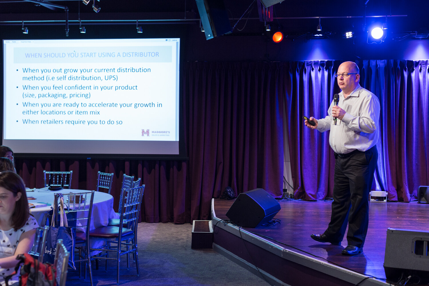 A presenter on stage beside a projected slide titled When should you start using a distributor.