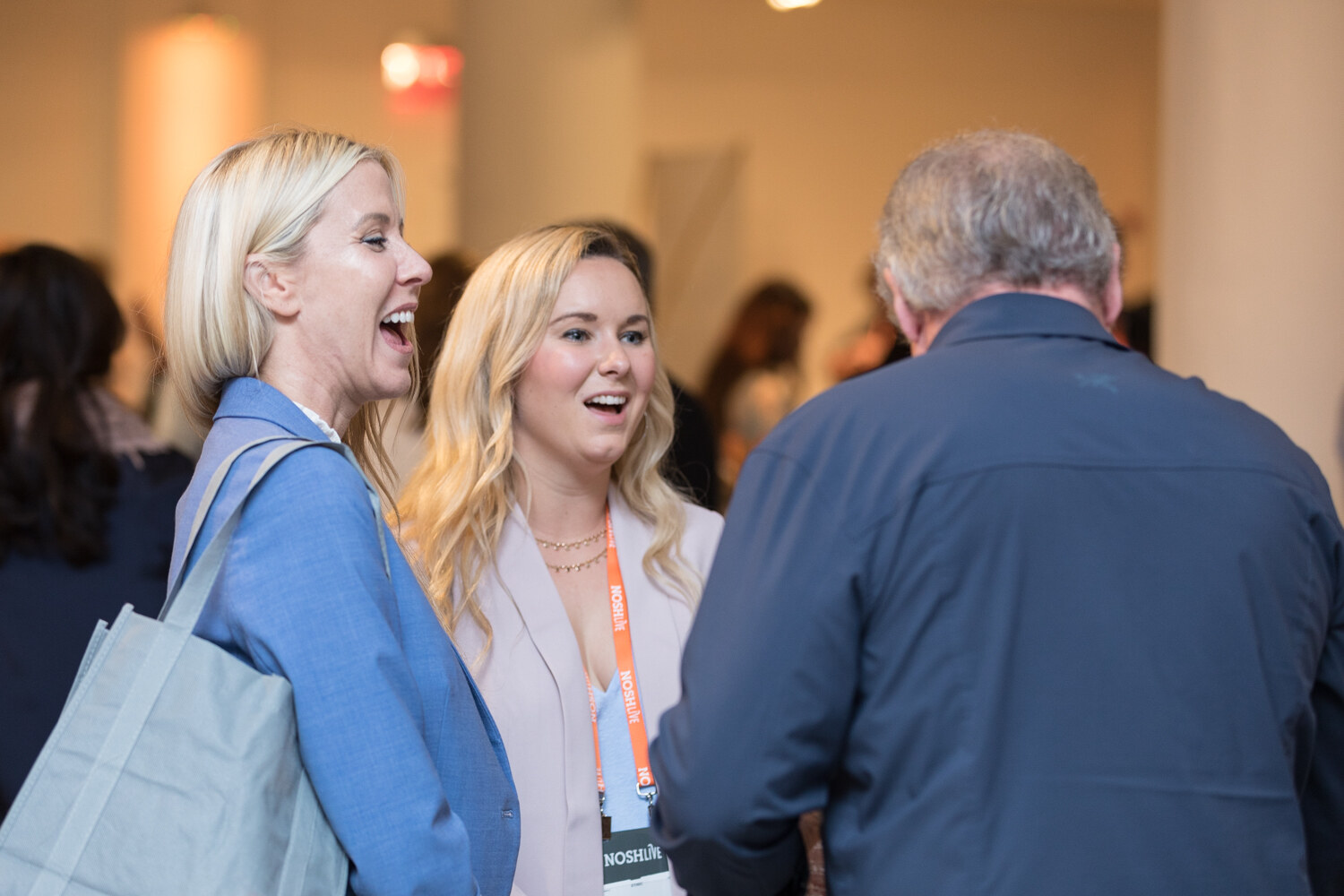 Two women laugh and talk with lanyards around their necks during the morning networking break.