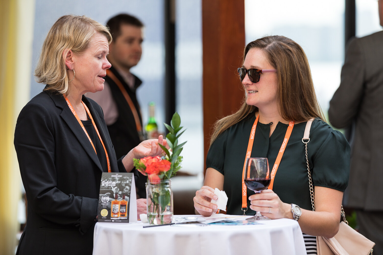Two women talk at a high-top table with a flower vase on the Hudson Terrace afterparty rooftop.