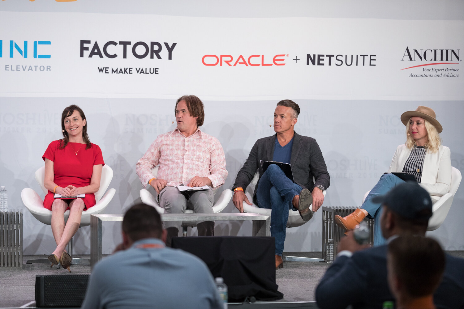 Wide view of the four Pitch Slam judges seated in white chairs in front of 301 Inc, Factory and Oracle NetSuite banners.