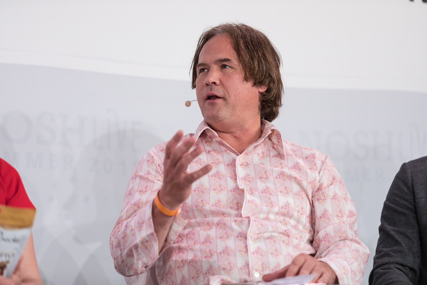 A Pitch Slam judge in a pink patterned shirt gestures while speaking.