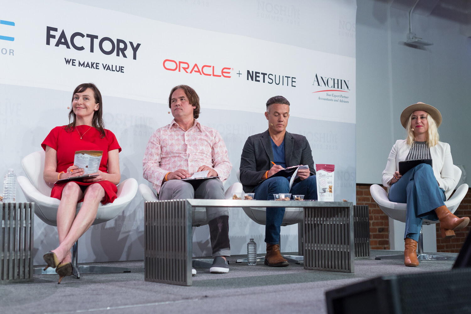 Low-angle view of four Pitch Slam judges seated in white chairs behind a metal table with snack samples.