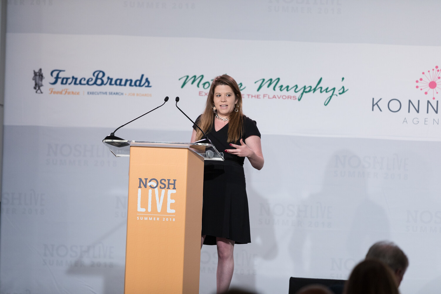 A speaker in a black dress presents at the NOSH LIVE lectern during The Investment Environment for Food Brands session.
