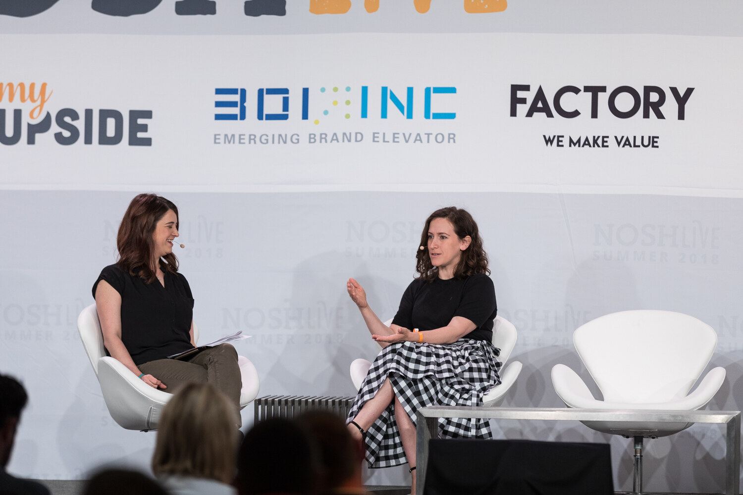 Wide view of two women seated on stage in front of sponsor banners during the Feedback, Failing Fast, and Flying High in Direct to Consumer session.