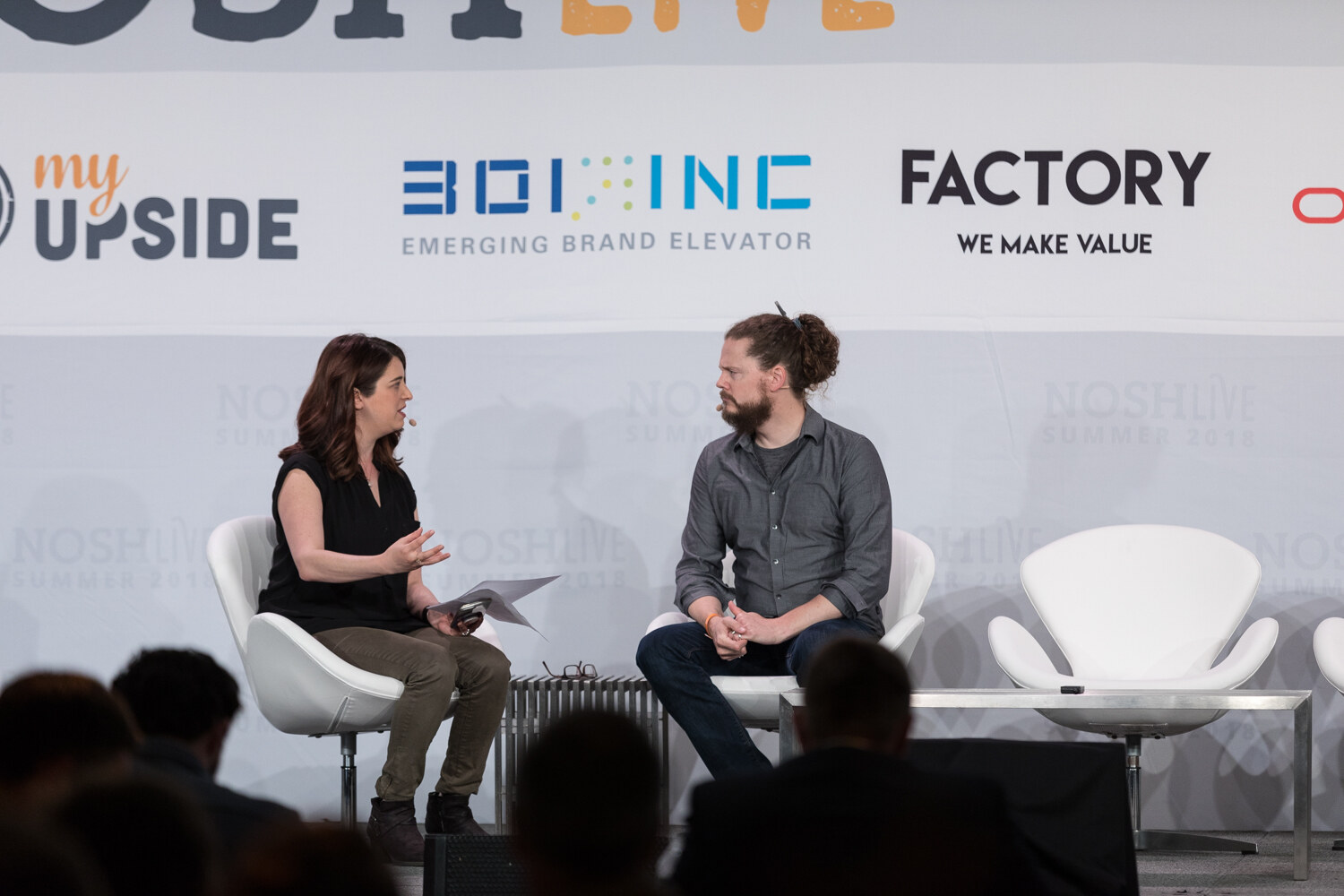 A moderator and a guest sit in white chairs on stage during the Unilever: Scaling Sustainability session.