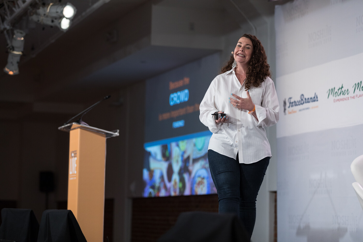 A presenter walks the stage beside the NOSH LIVE lectern with a projected slide at left during the Lessons from Crowdfunded Brands session.