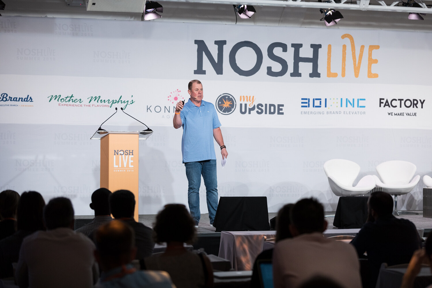 Wide view of a presenter at the NOSH LIVE stage with the audience in silhouette during the Roles Meet Revenue session.