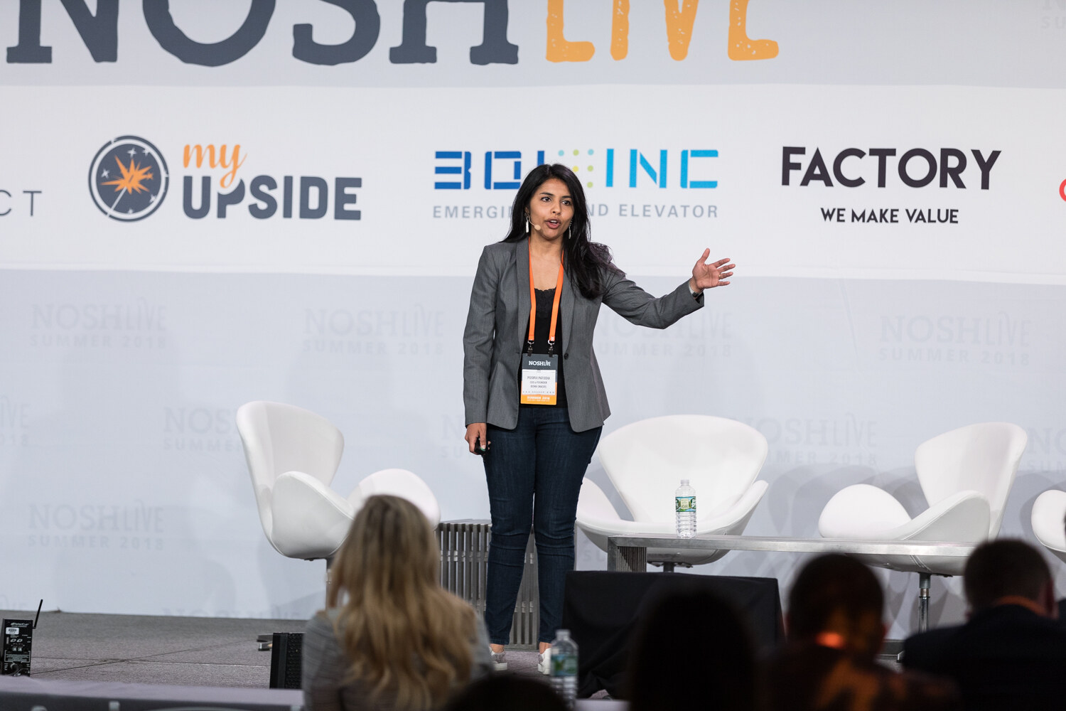 A presenter in a gray blazer and conference lanyard speaks on the Nosh Live stage during the From the Frontlines session.