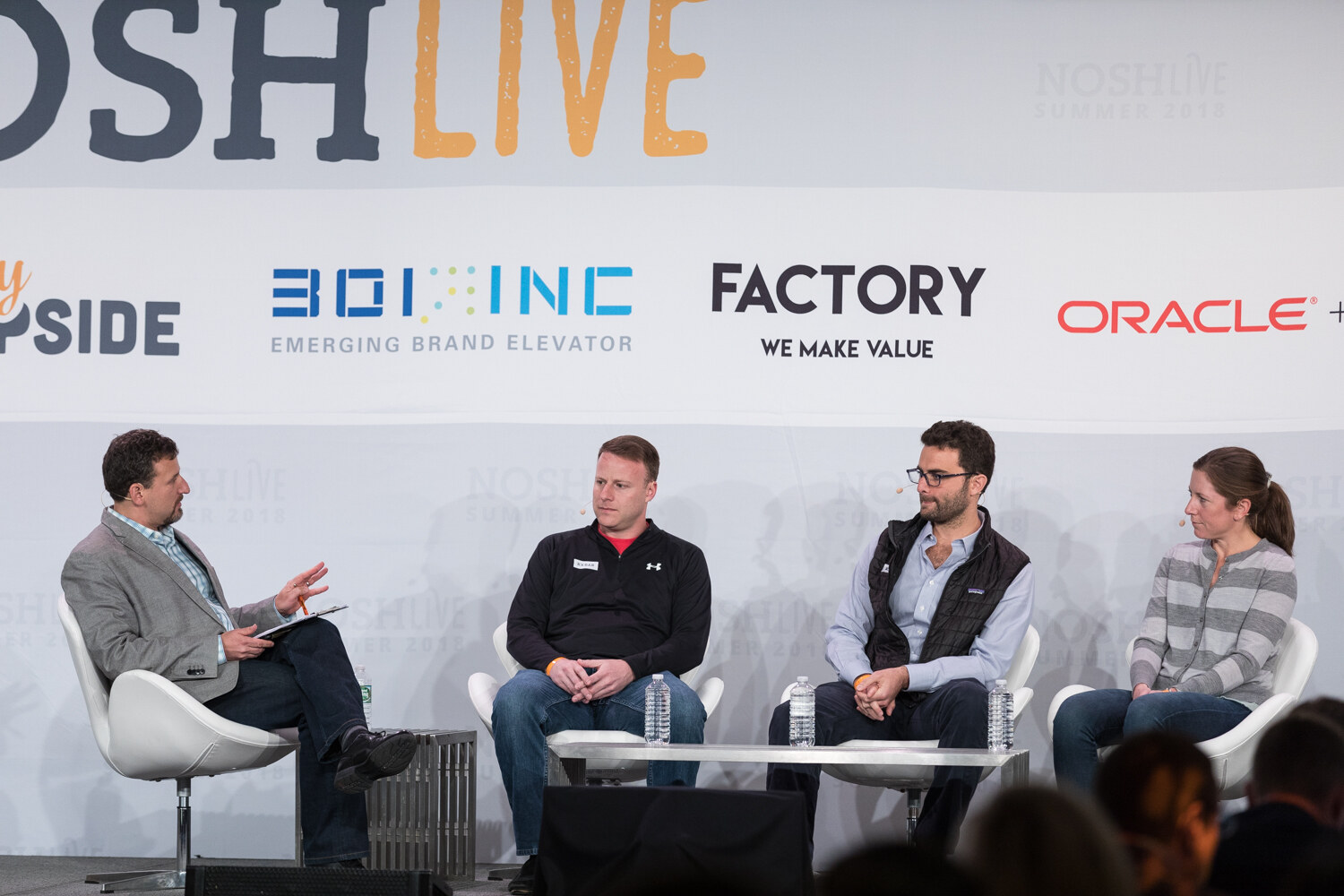 A moderator and three panelists sit in white chairs on stage during the Big Deal session.