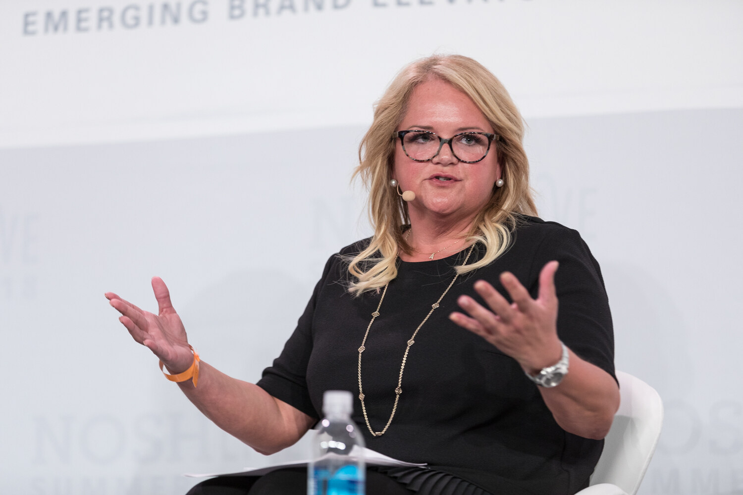 A guest in a black top and glasses gestures with both hands while seated on stage during the Innovation session.