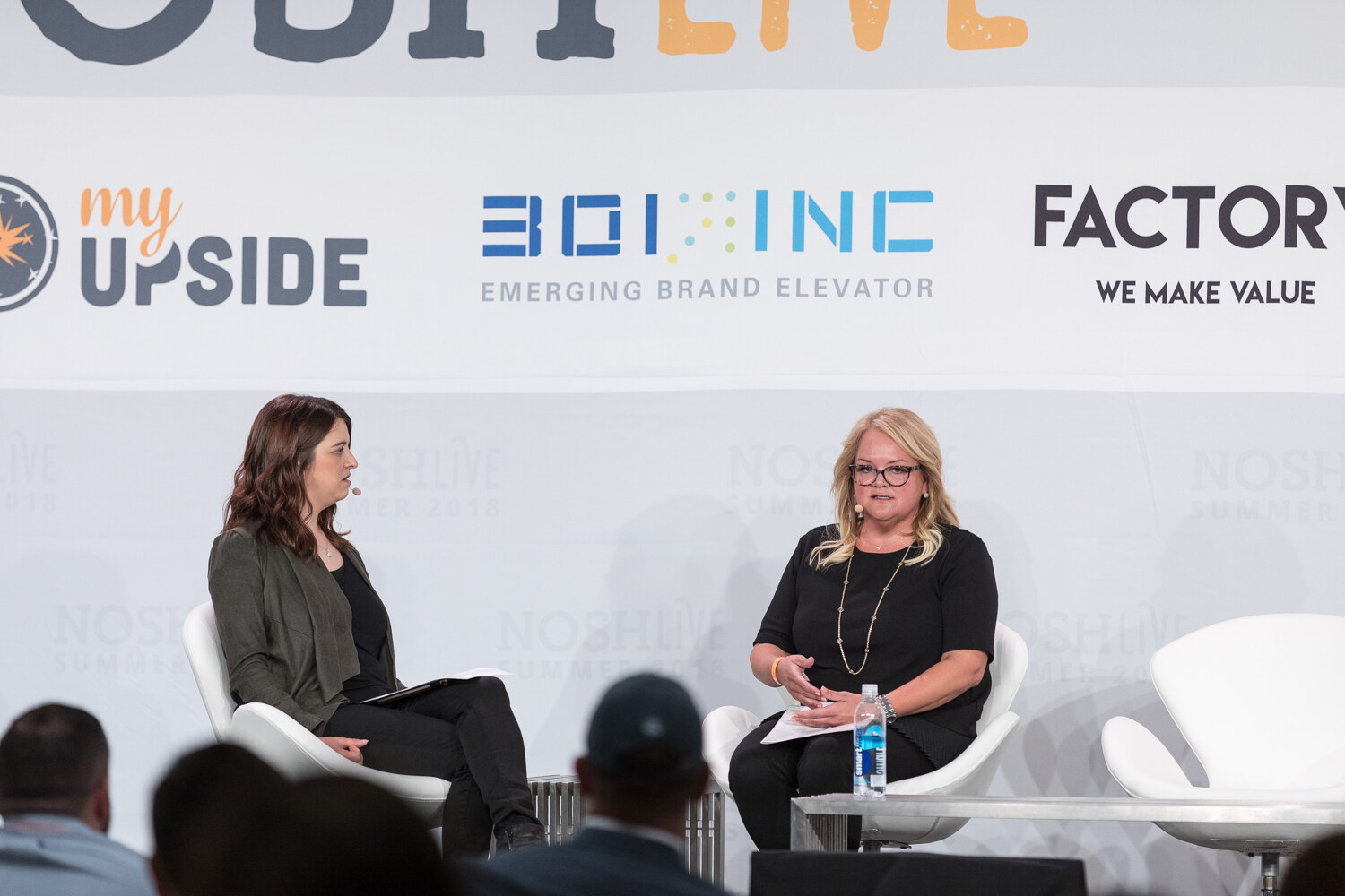 A moderator and a guest sit in white chairs on stage in front of My Upside and 301 Inc banners during the Innovation session.
