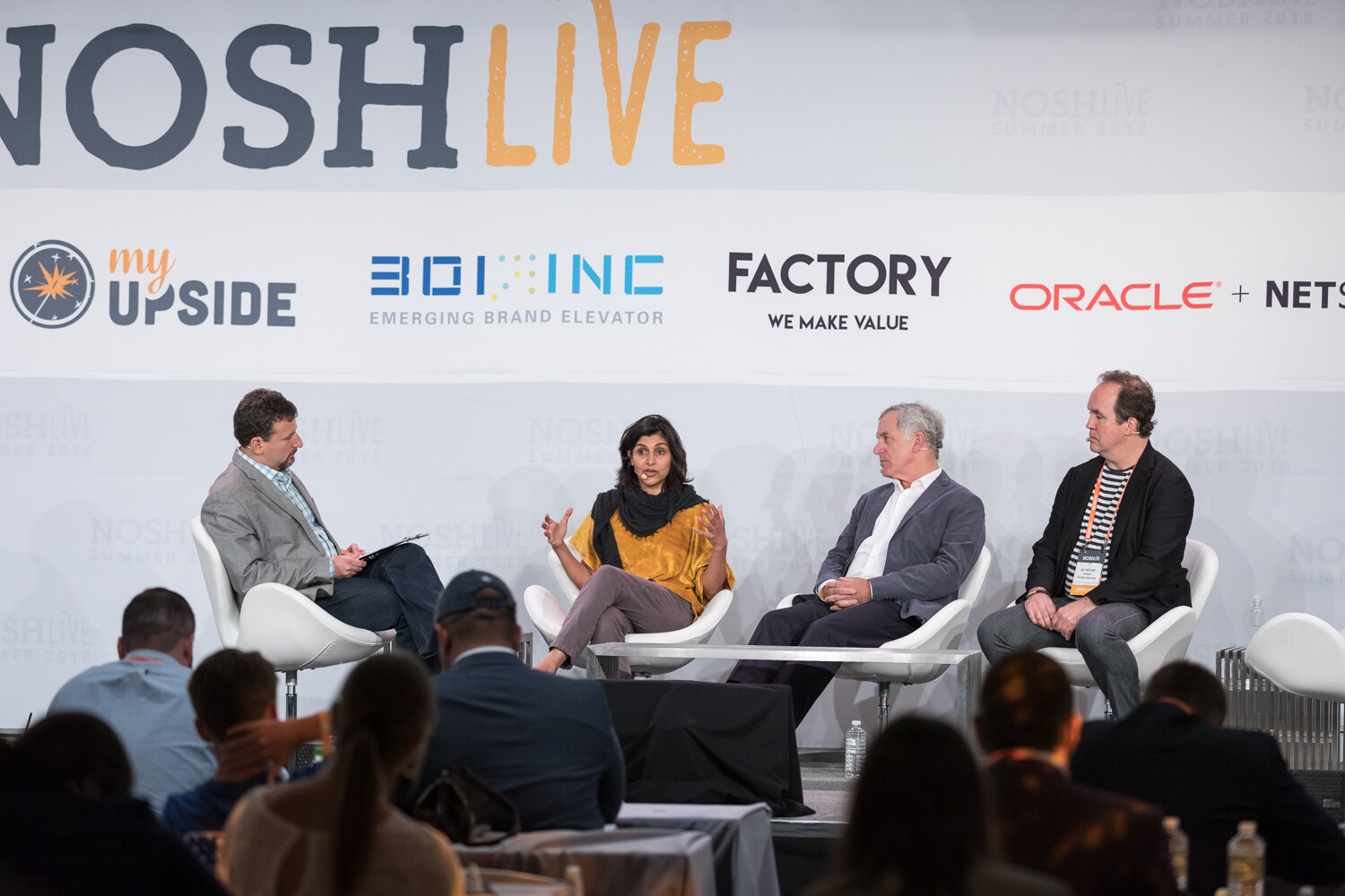 Wide view of a moderator and three panelists seated on stage with the audience in the foreground during the Wrap-Up.