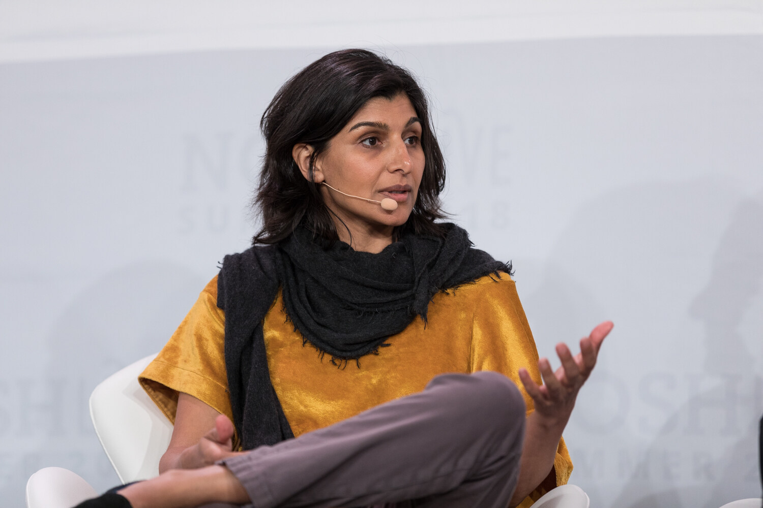 A panelist in a mustard top and black scarf gestures while seated during the Wrap-Up.