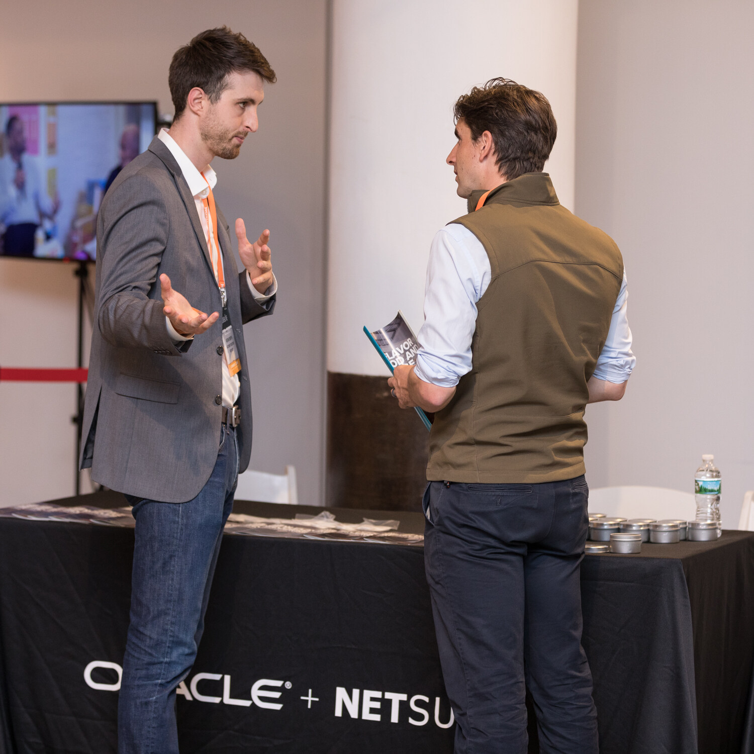 Two men talk beside a black table covered with an Oracle NetSuite tablecloth.