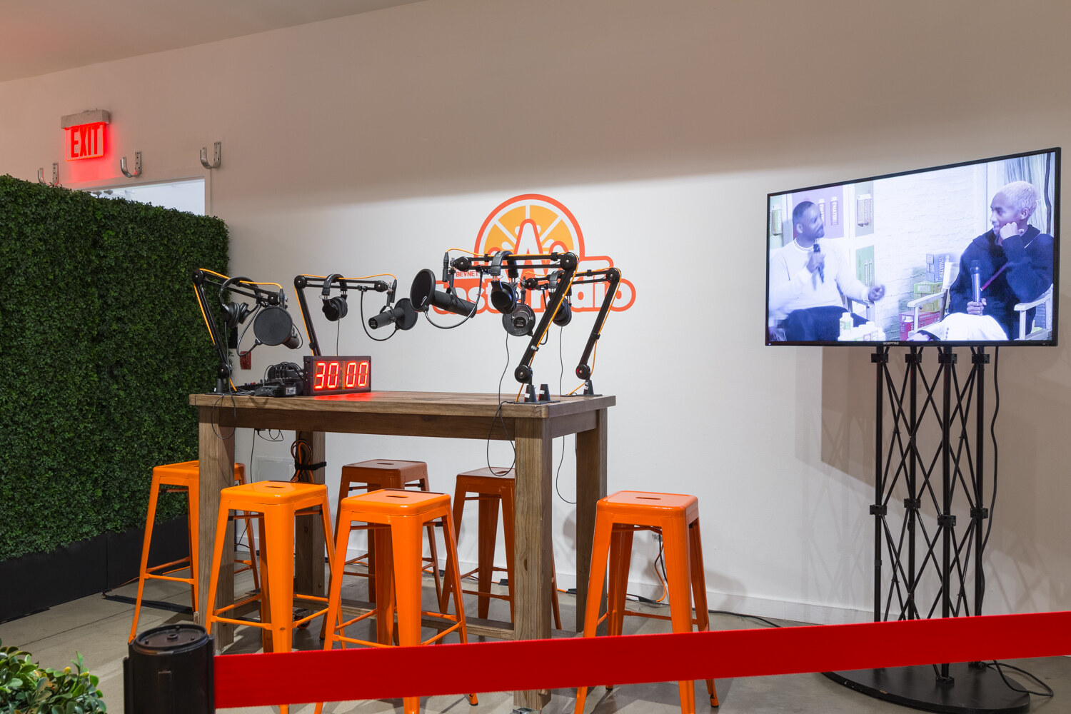 The Taste Radio podcast corner set up with orange stools, microphones, a wall screen and a countdown timer.