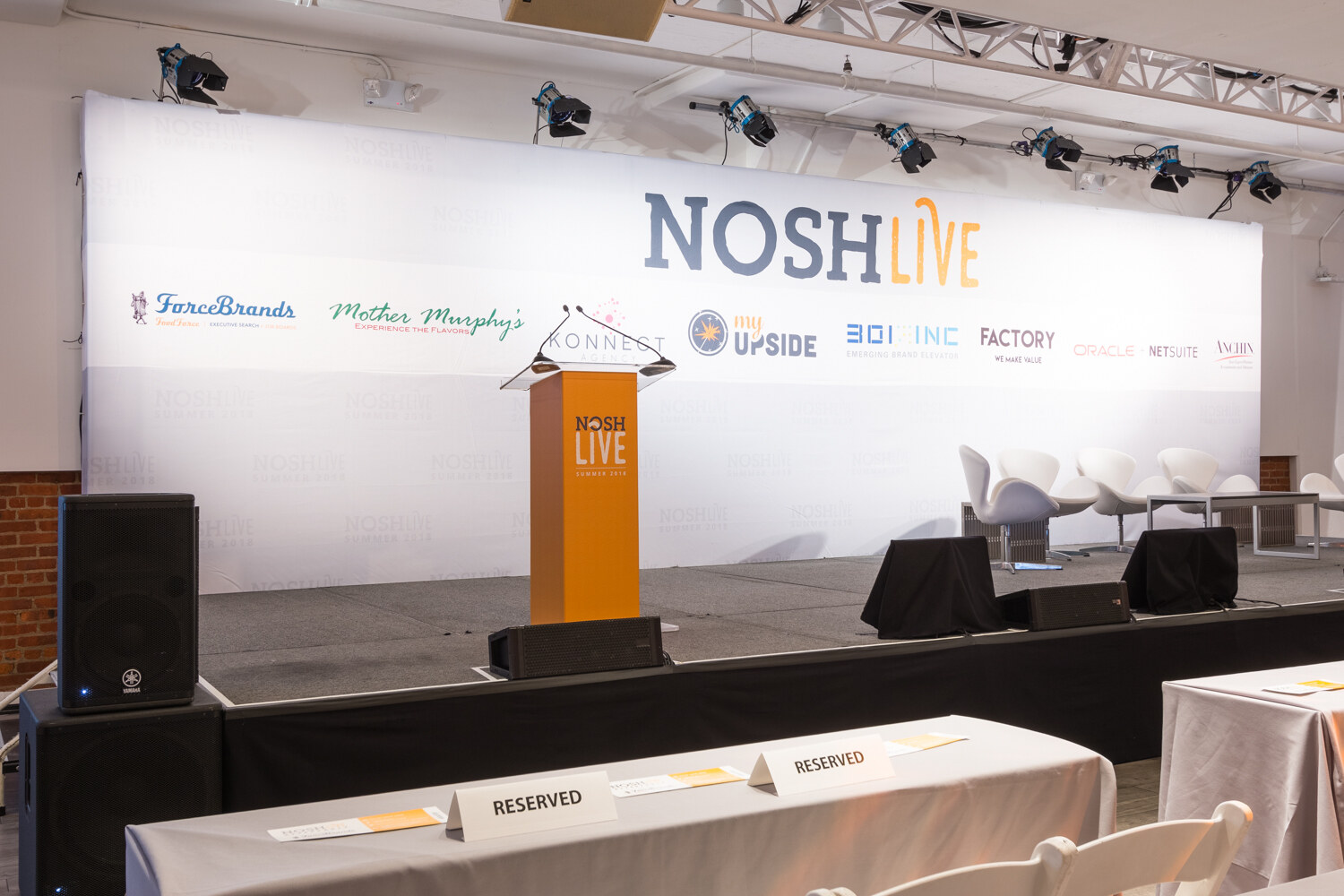The empty Nosh Live main stage with a lectern, sponsor backdrop and reserved front-row tables before doors opened.