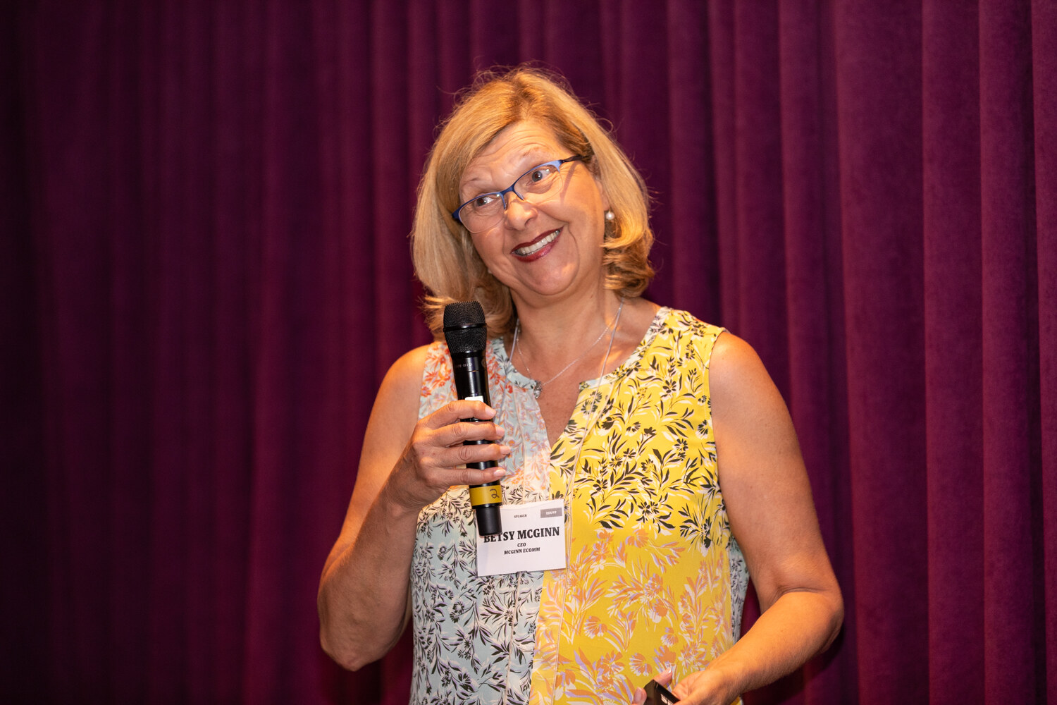 Boot Camp speaker in a yellow and gray sleeveless top smiling while holding a microphone