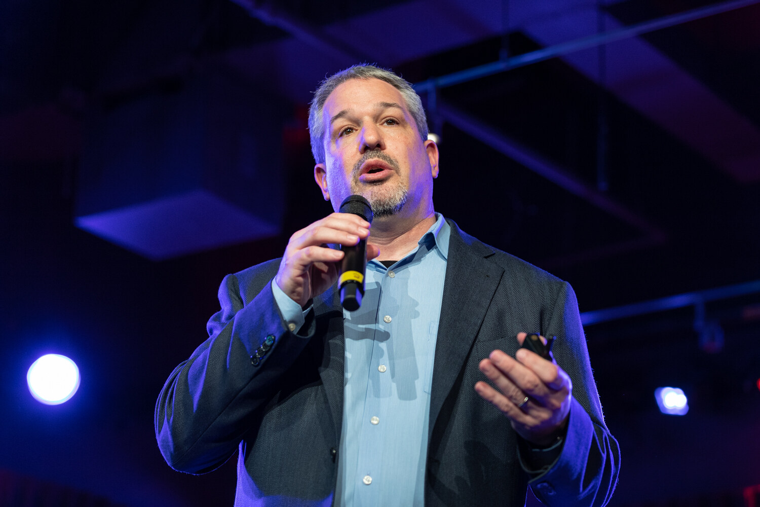 Boot Camp speaker with gray hair in a navy blazer and light blue shirt speaking into a microphone with a clicker in hand