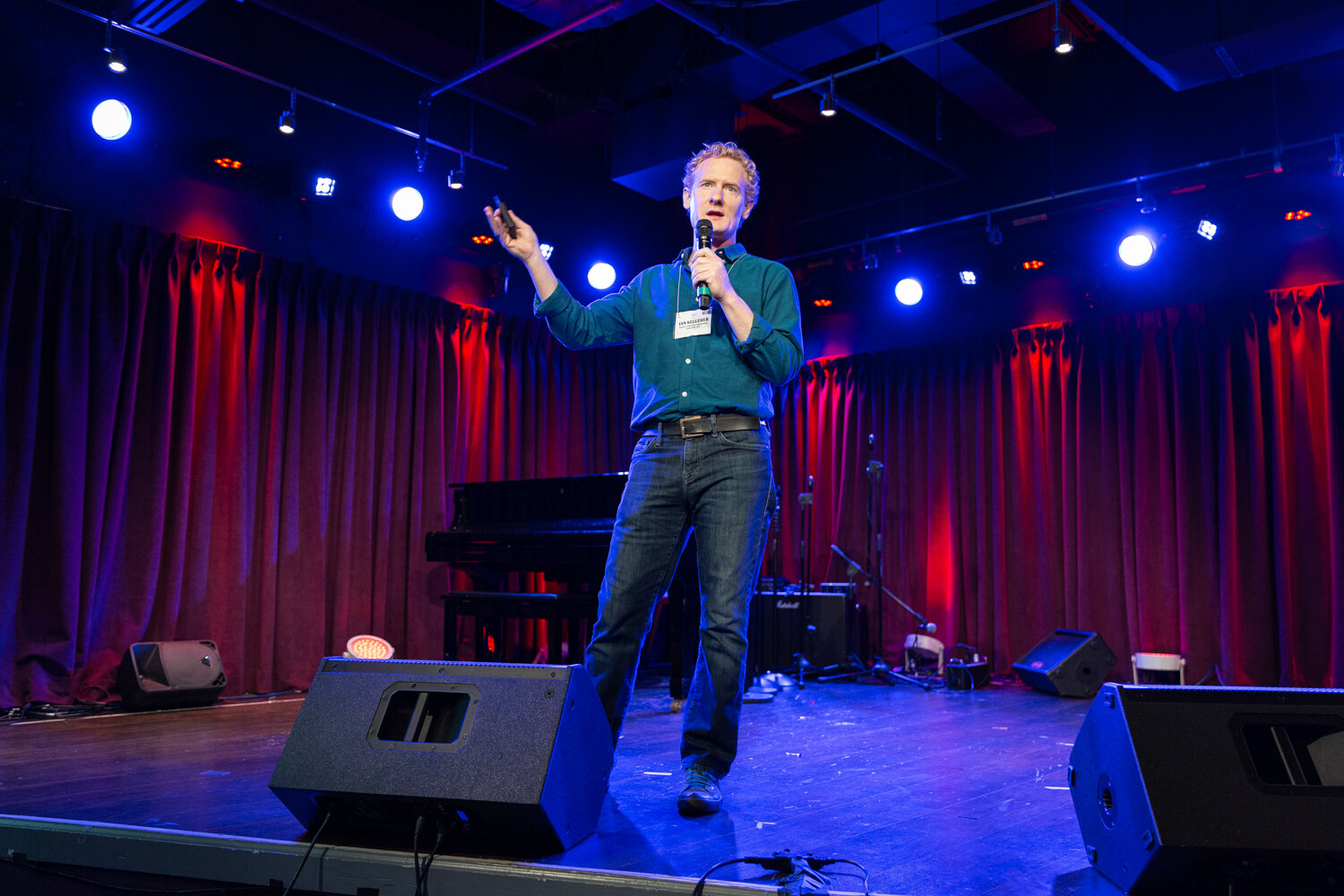 Boot Camp speaker in a teal shirt striding across the stage with one arm raised under blue lights