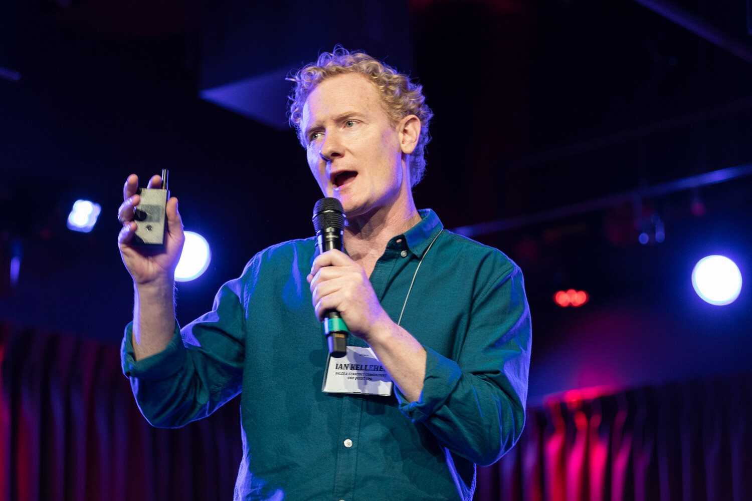 Boot Camp speaker in a teal shirt raising a clicker while speaking into a microphone