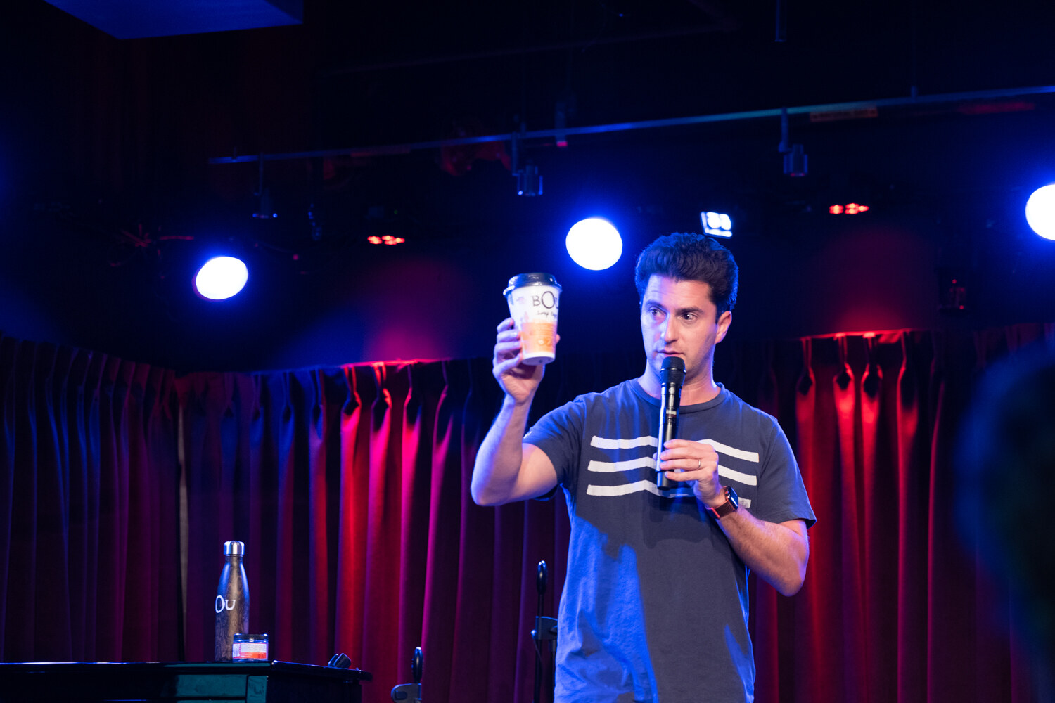 Boot Camp speaker in a gray striped T-shirt holding up a coffee cup while speaking