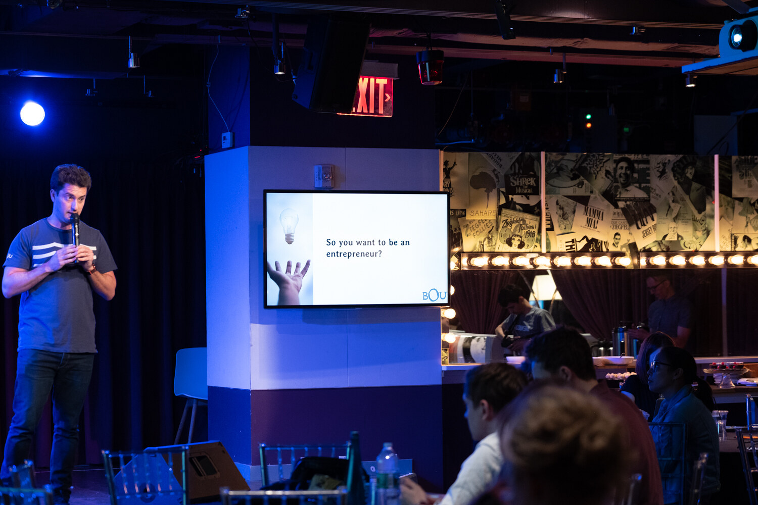 Boot Camp speaker beside a wall screen reading So you want to be an entrepreneur