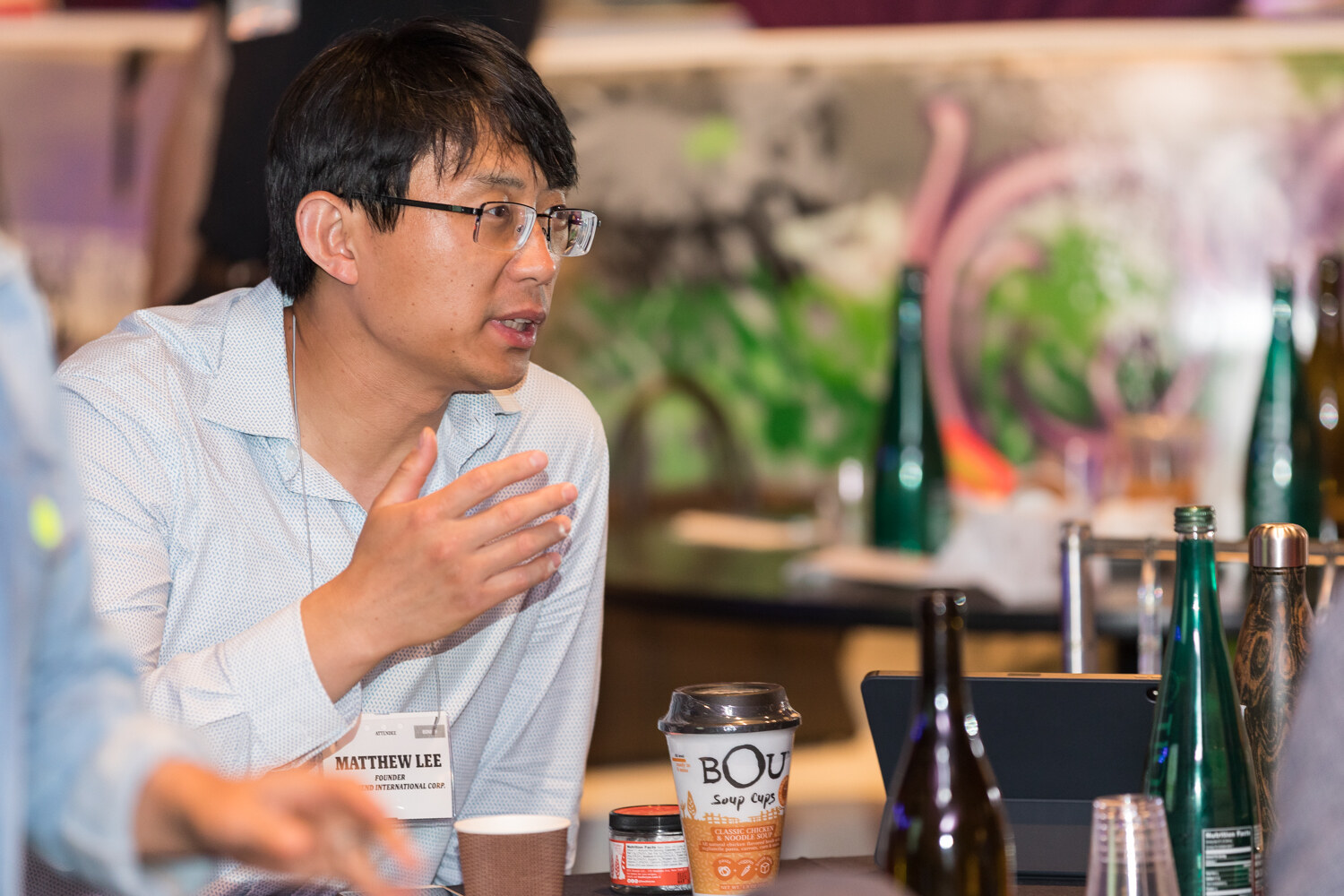 Man in glasses gesturing as he talks at a Boot Camp table beside a BOU cup