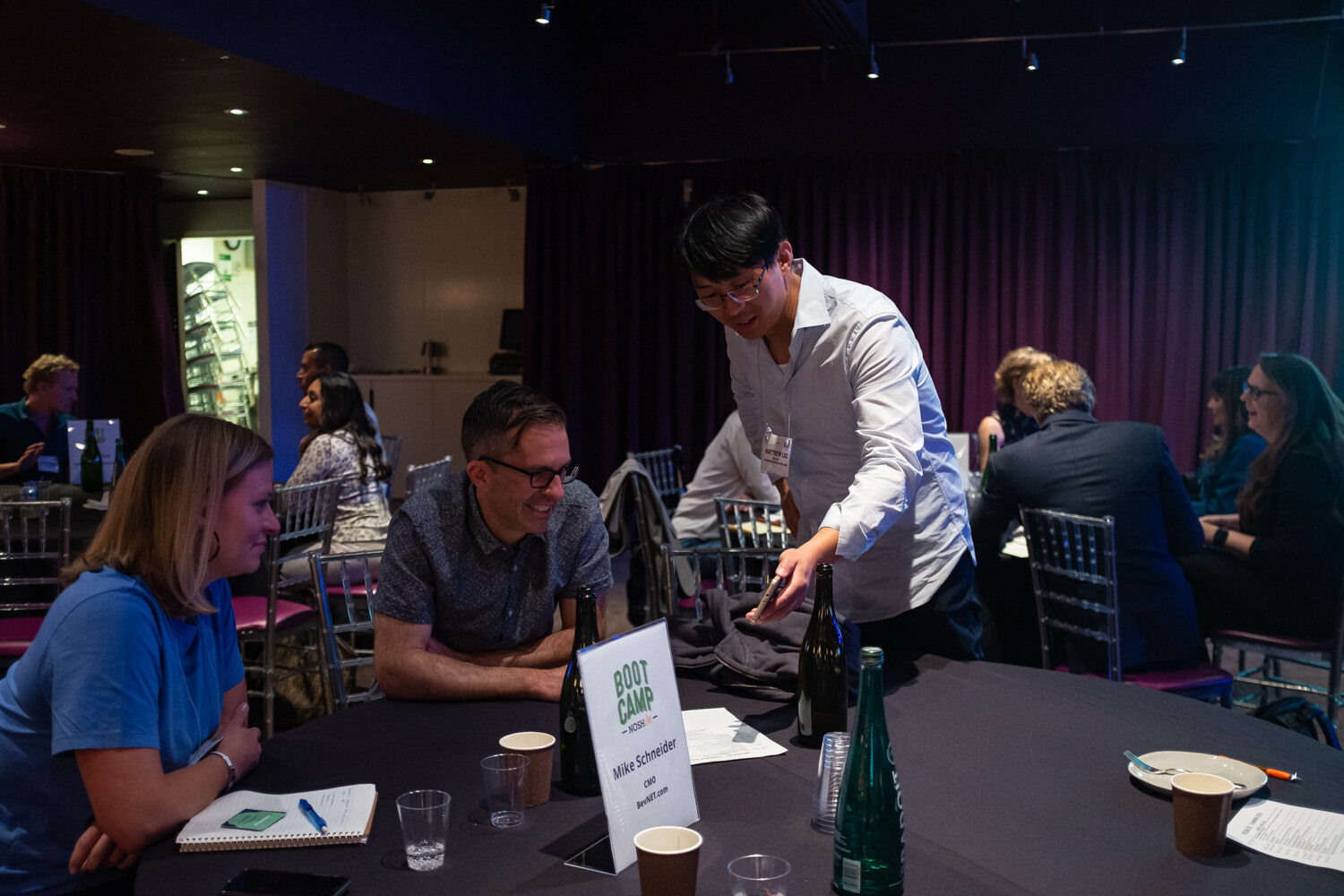 Man leaning over a Boot Camp mentor table to talk with seated attendees