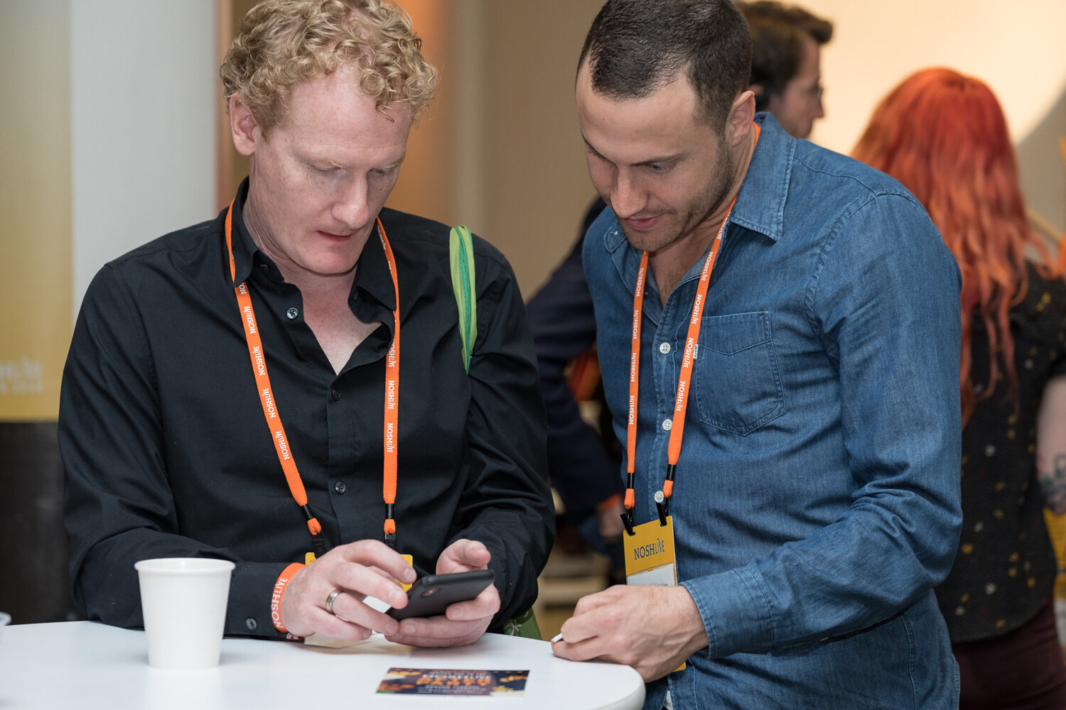 Two men looking at a phone at a high-top table