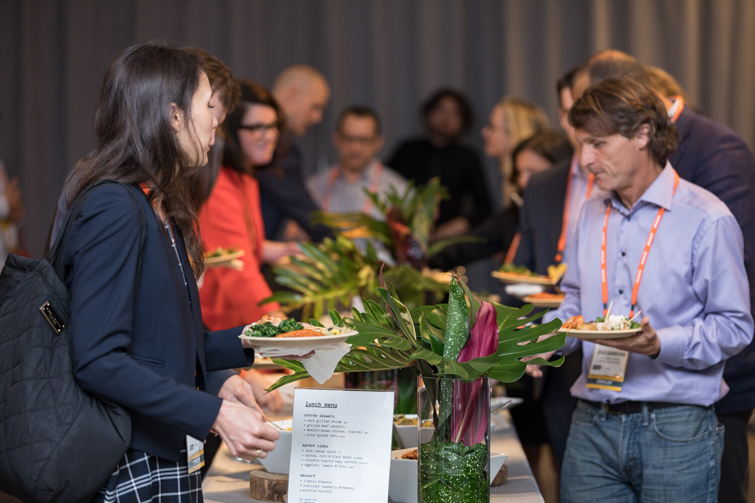 Attendees serving themselves from the lunch buffet beside tropical leaf decor