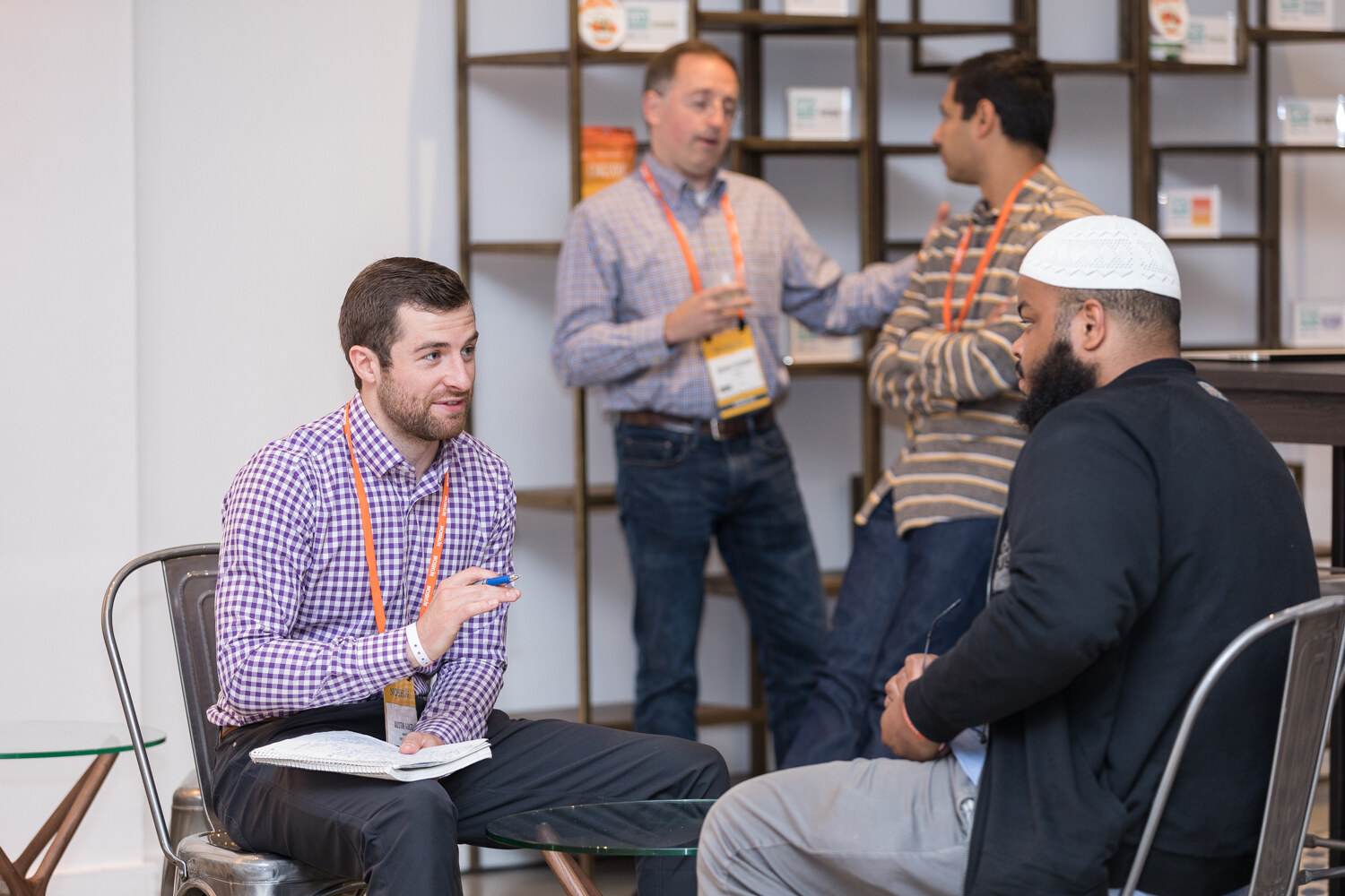 Attendees talking in a lounge area with a shelving wall behind them