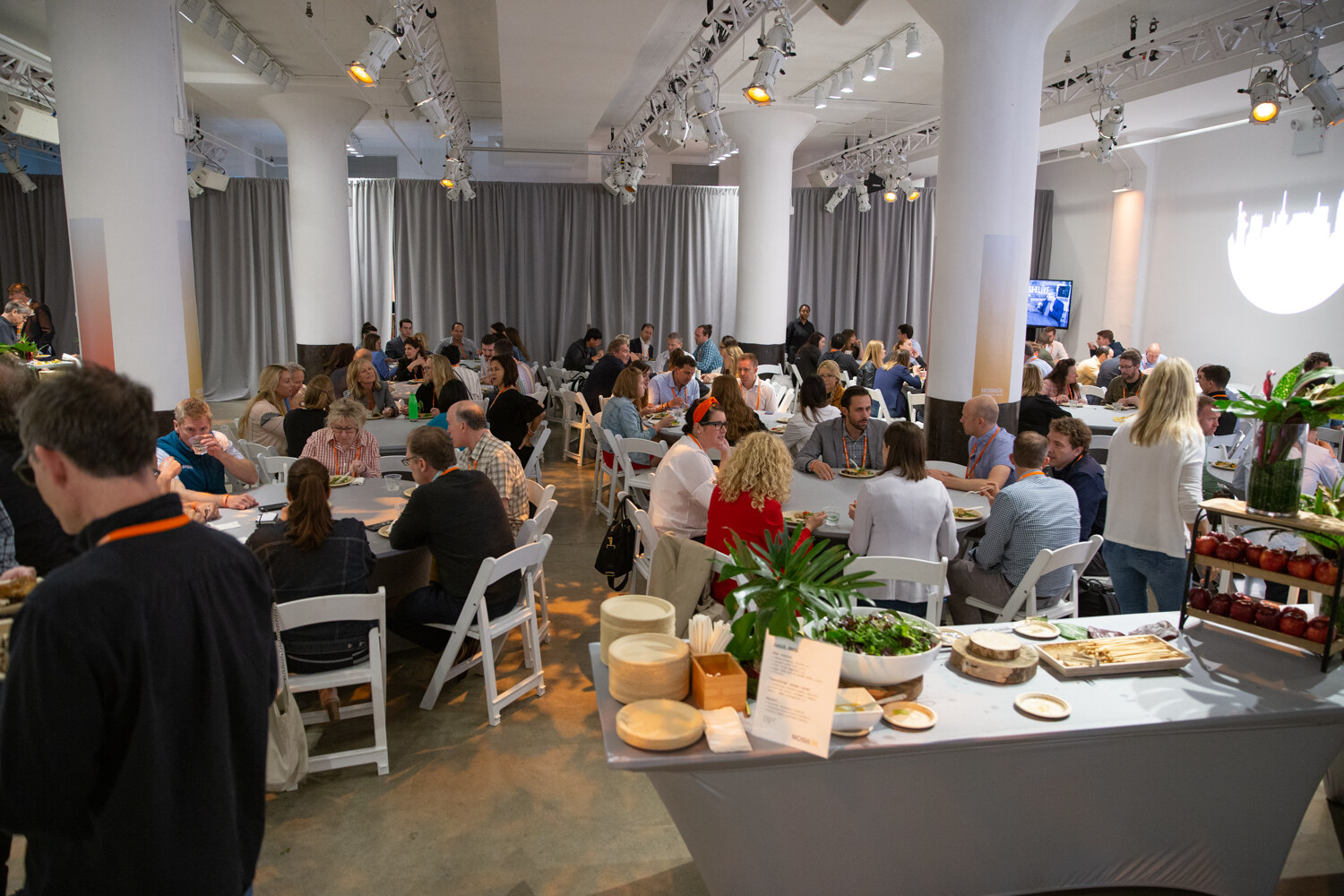 Lunch hall with attendees at round tables and a catering buffet on the right