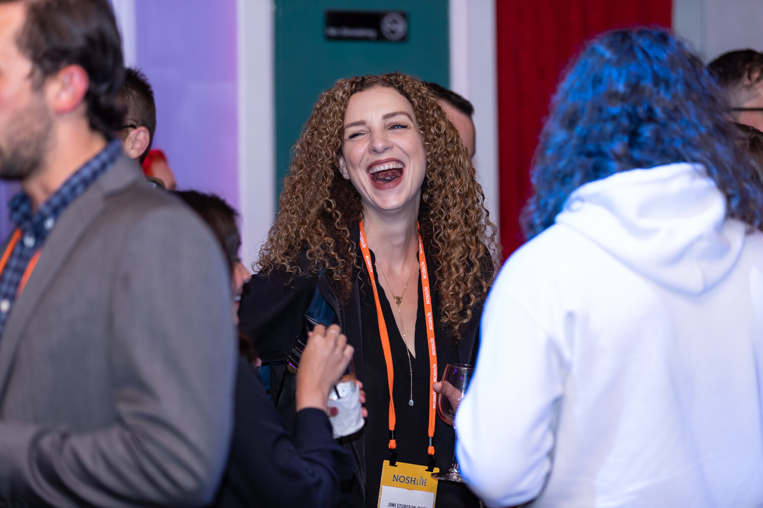 Woman with long curly hair laughing among guests, one in a white hoodie