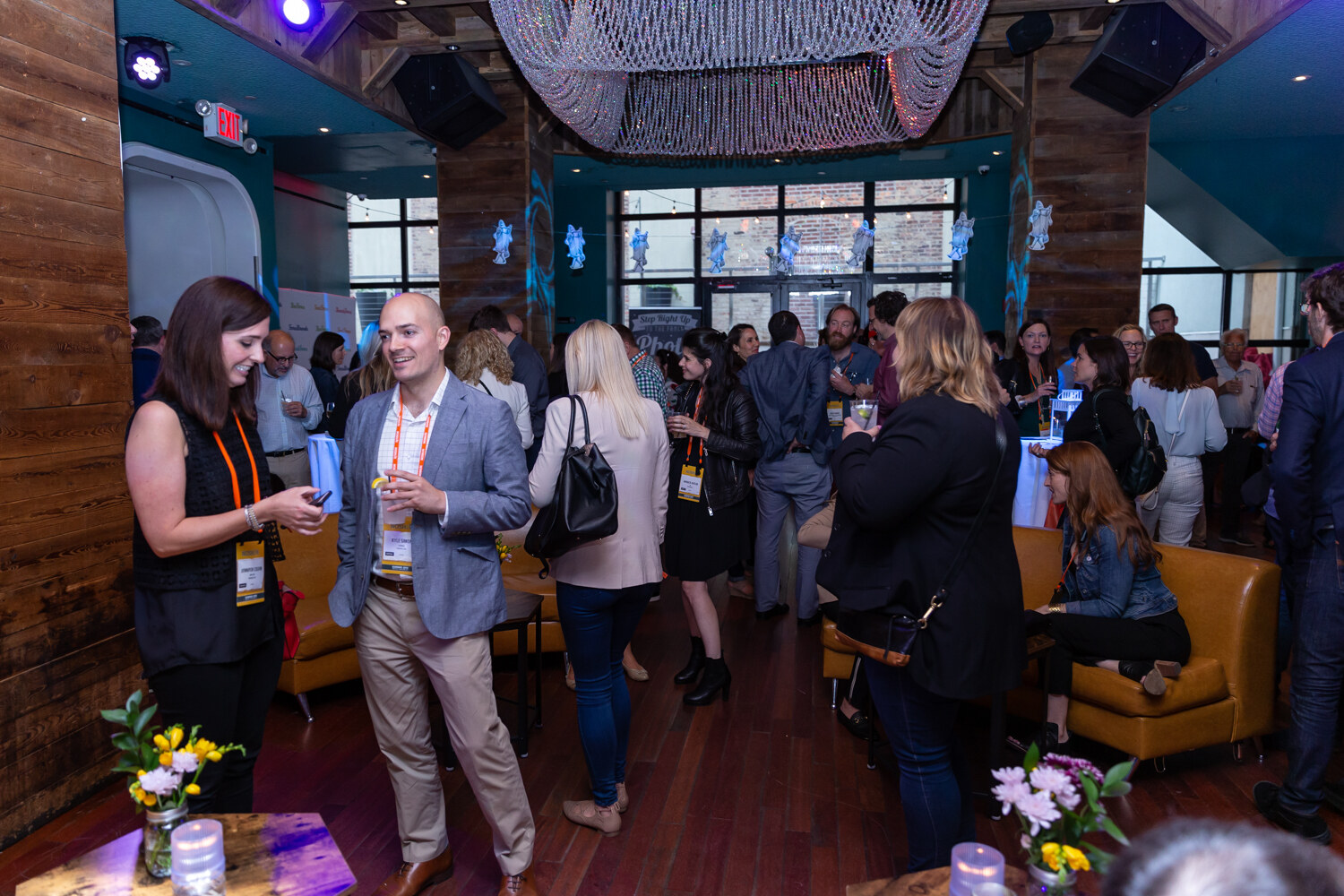 Guests mingling beside orange leather banquettes under a beaded chandelier in the After Party room