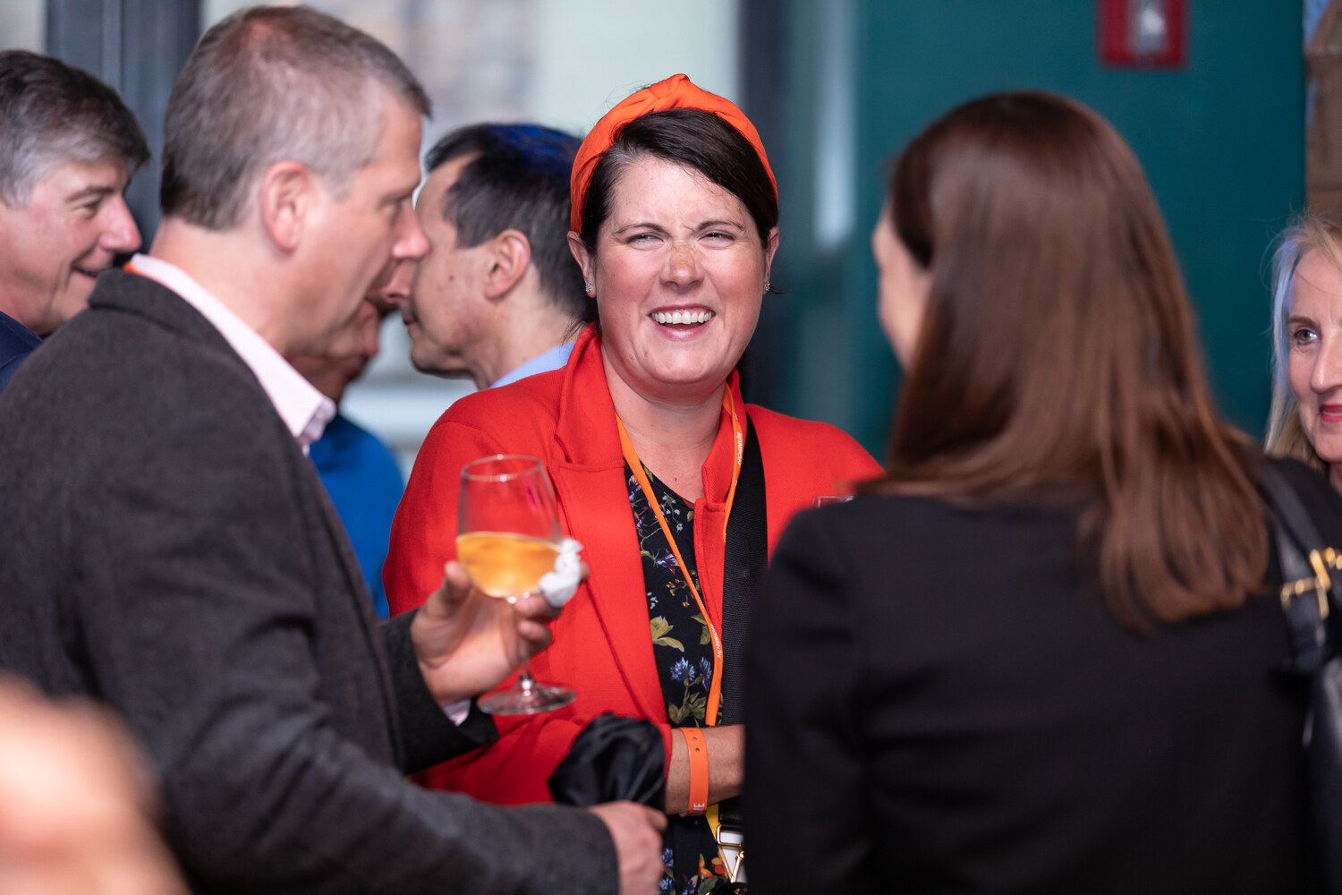 Woman in a red blazer and orange headband laughing with a glass of wine