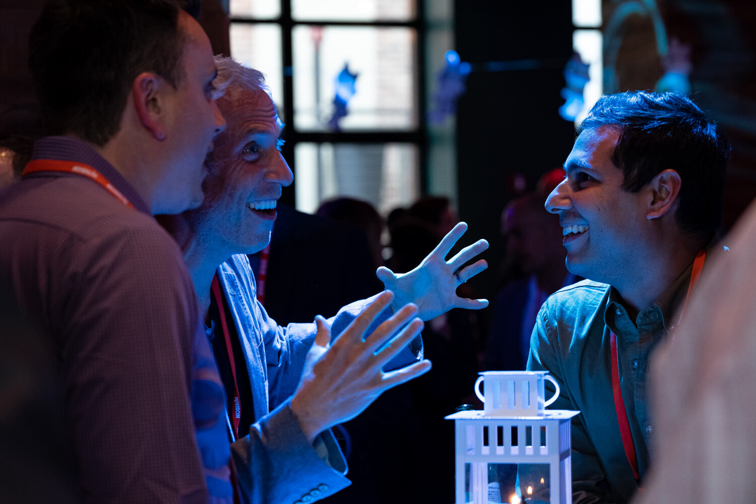 Two men laughing and gesturing in conversation beside a white lantern