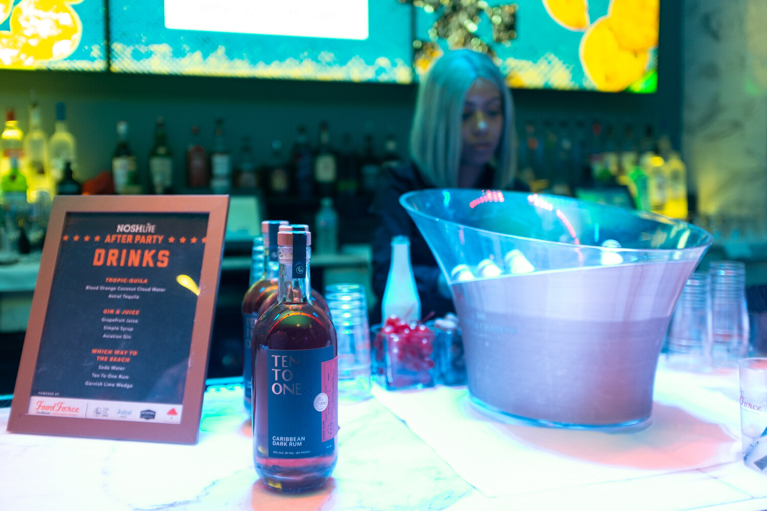 NOSHLIVE After Party drinks menu beside bottles and a bucket of ice on the bar