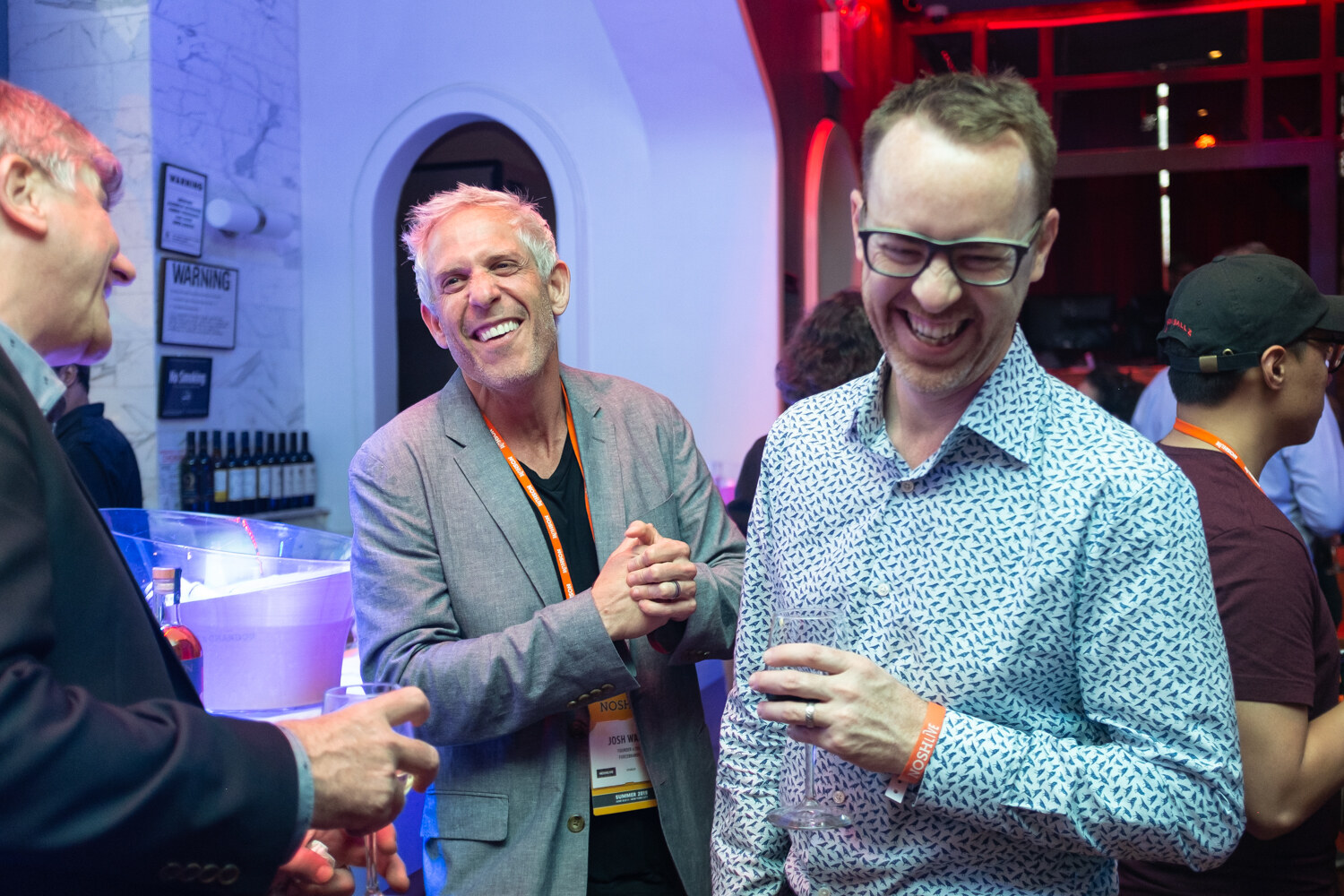 Two men laughing together, one in a gray blazer and one in a patterned shirt