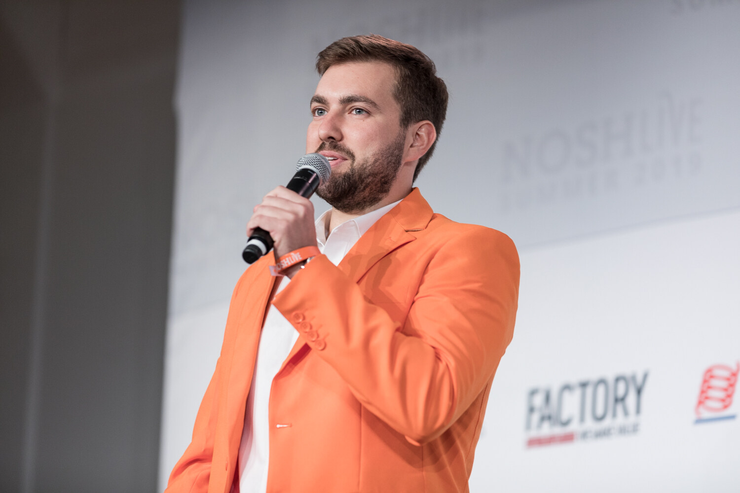 Pitch Slam presenter in an orange blazer speaking into a microphone in close view