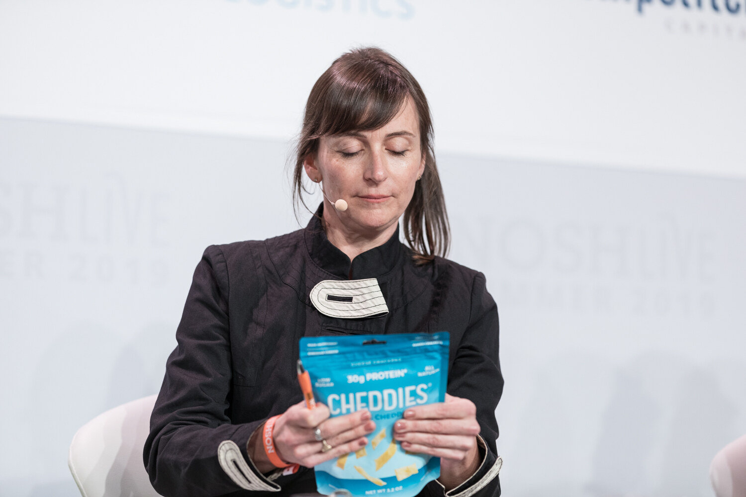 Judge in a black jacket with ponytails reading a bag of Cheddies protein chips