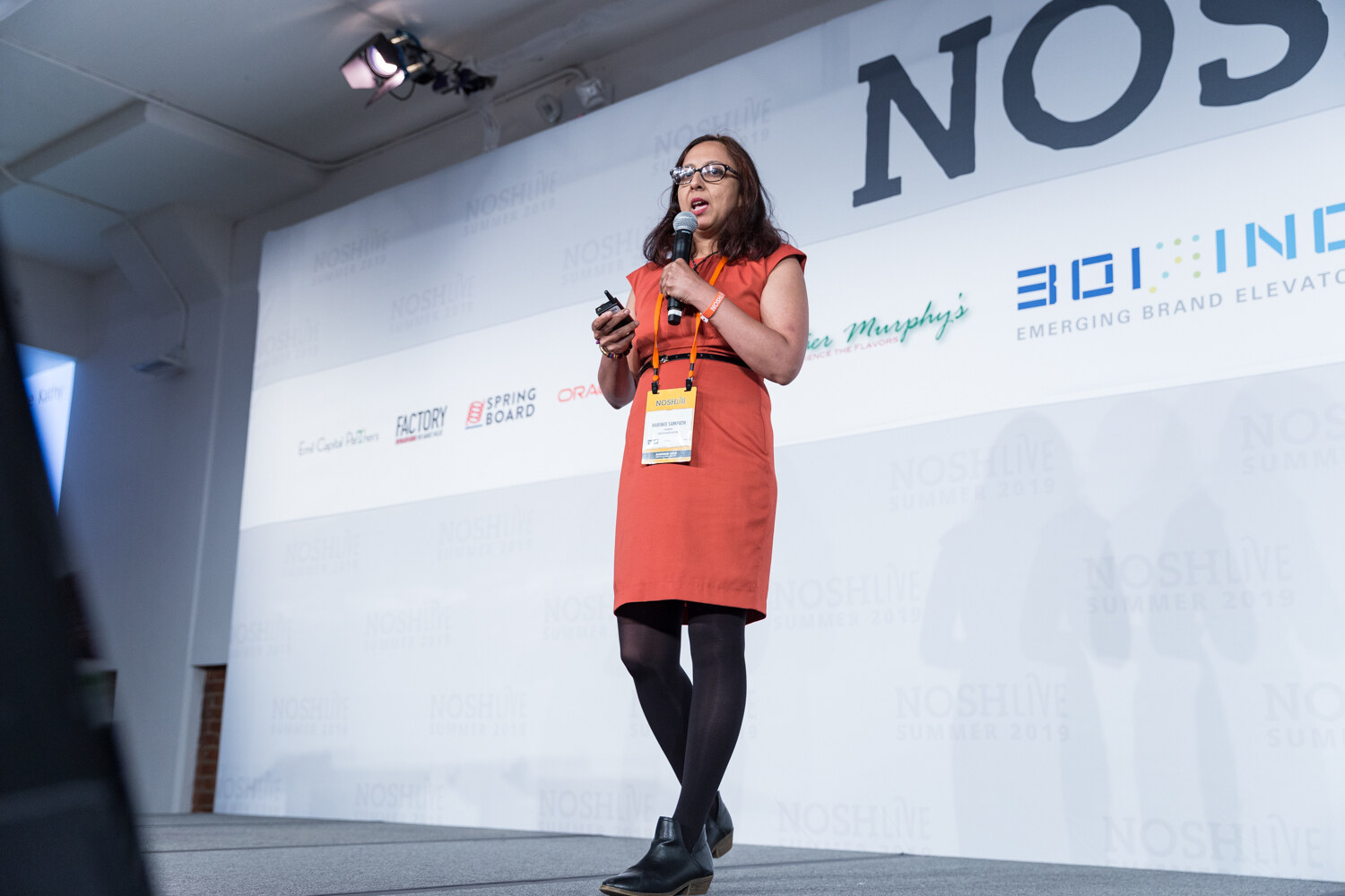 Pitch Slam presenter in a coral dress with a lanyard walking across the stage while speaking