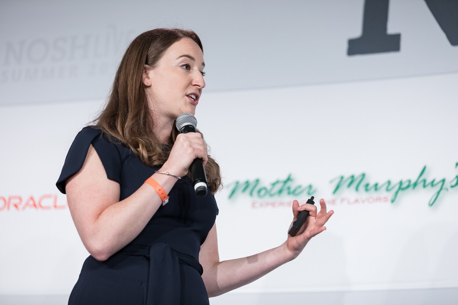 Pitch Slam presenter in a navy jumpsuit pitching with a microphone in front of the Mother Murphy's logo