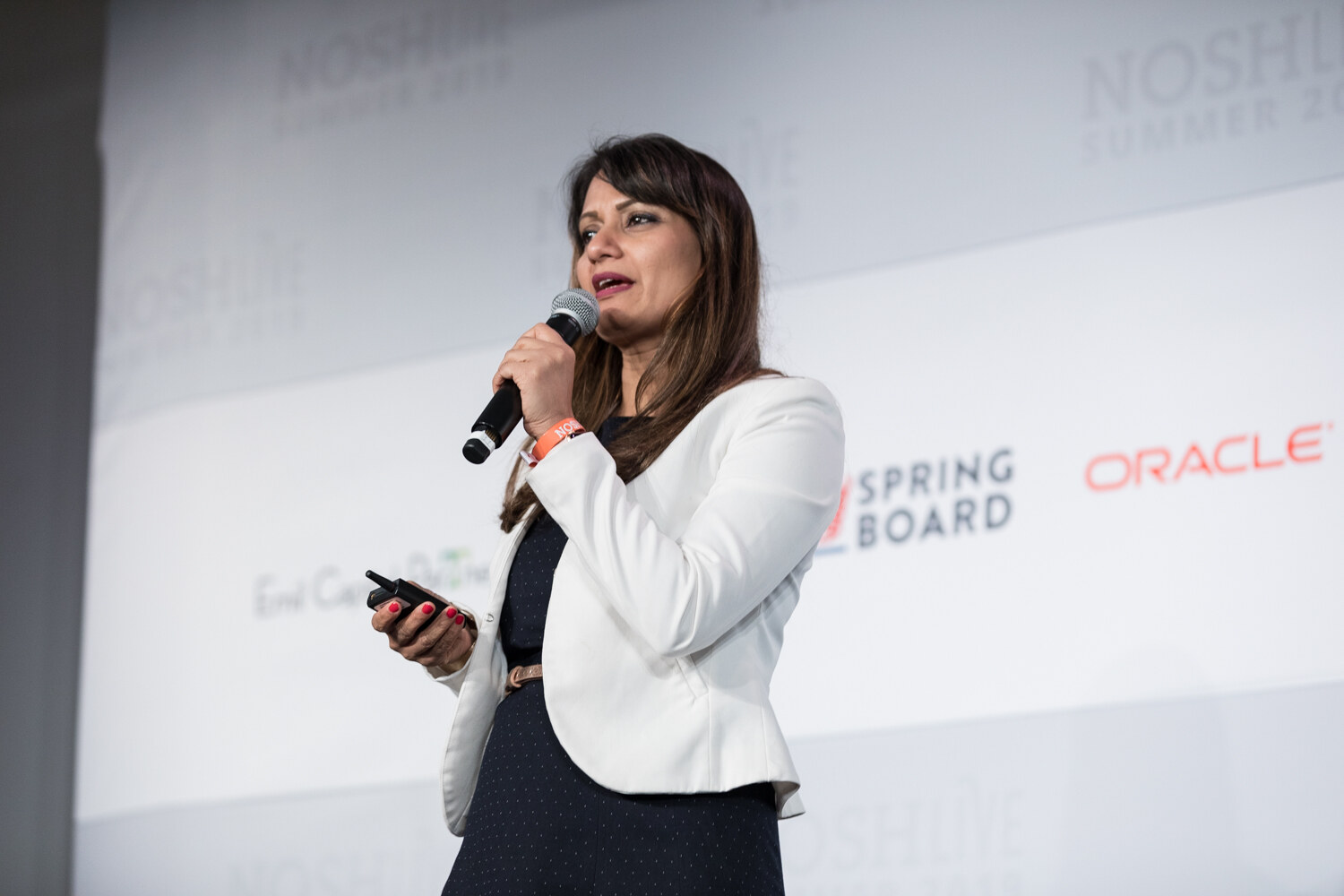 Pitch Slam presenter in a white blazer and navy dress speaking into a microphone