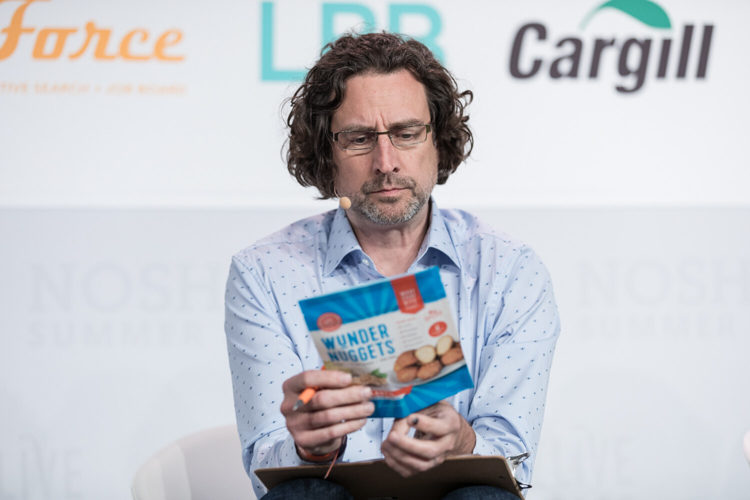 Curly-haired judge in a light blue shirt reading a bag of Wunder Nuggets