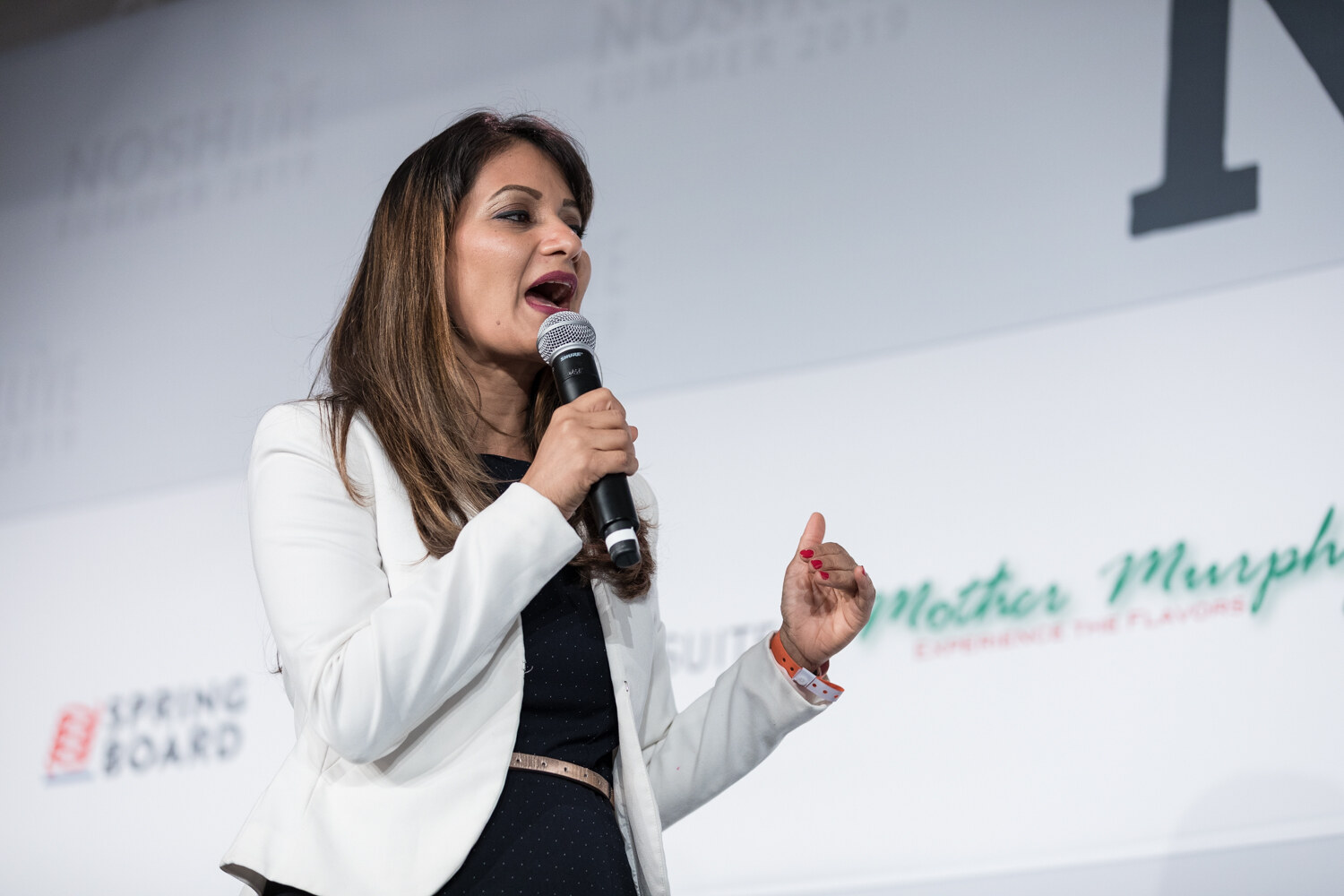 Pitch Slam presenter in a white blazer gesturing mid-pitch